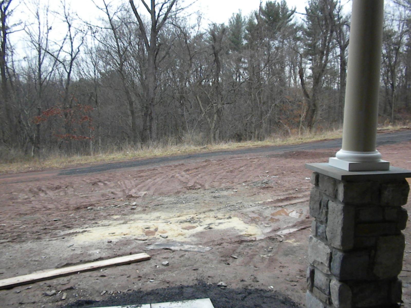 A porch column on its stone pier seen from the yard, bare woods and rutted earth beyond