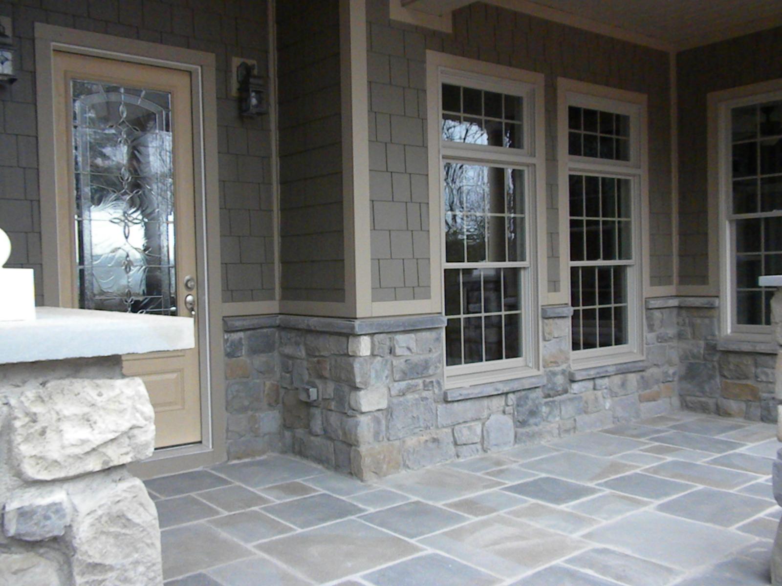 The covered porch along the front, flagstone underfoot and stone piers between the windows