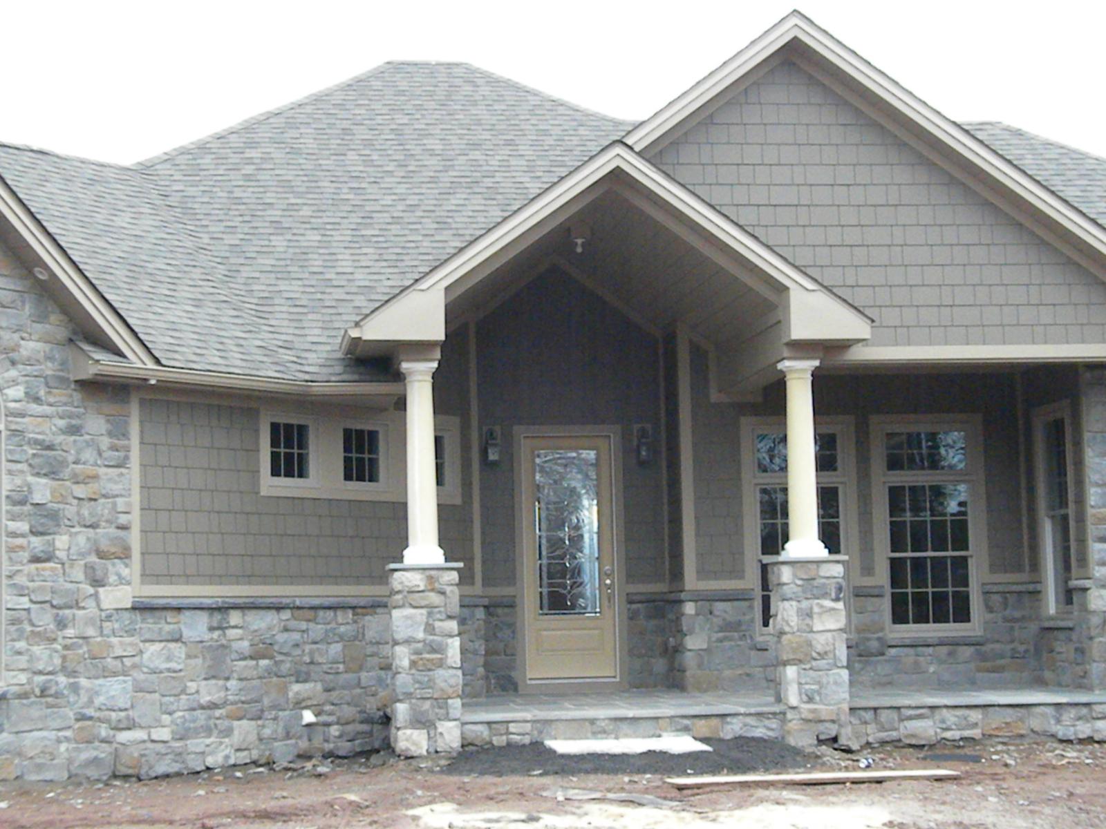 The entry close to, tapered columns on cut-stone piers carrying the porch gable, a paneled door with a leaded light between them