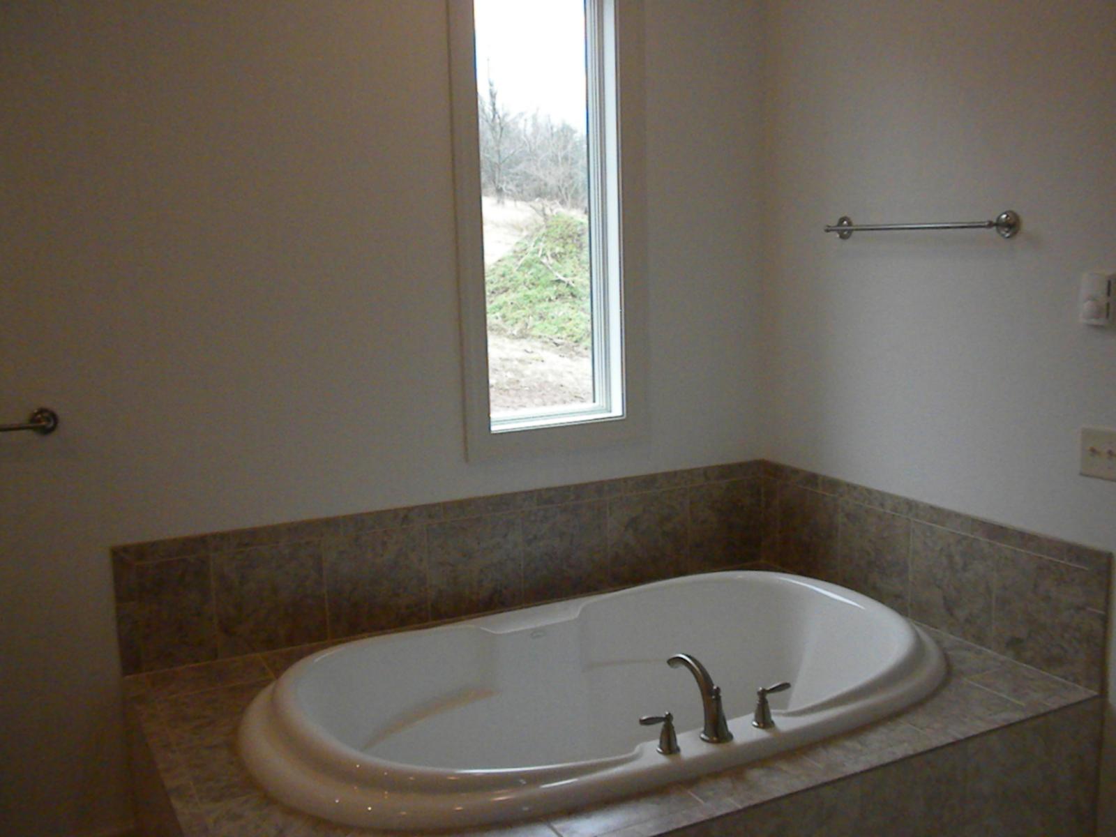 A soaking tub set into a tiled deck beneath a window looking out to bare woods