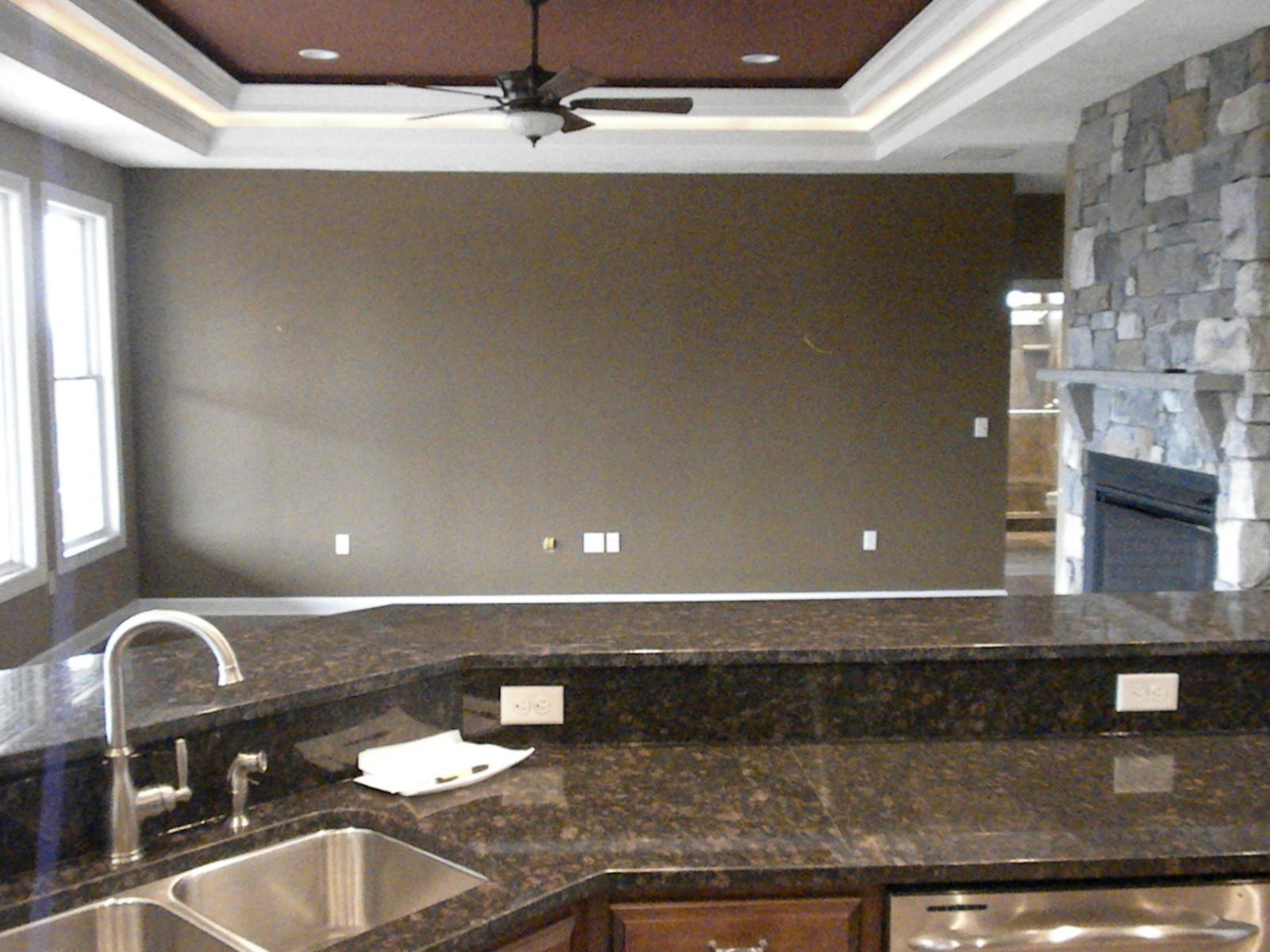 The kitchen counter run and sink, tray ceiling with a fan above and the stone chimney visible past the corner