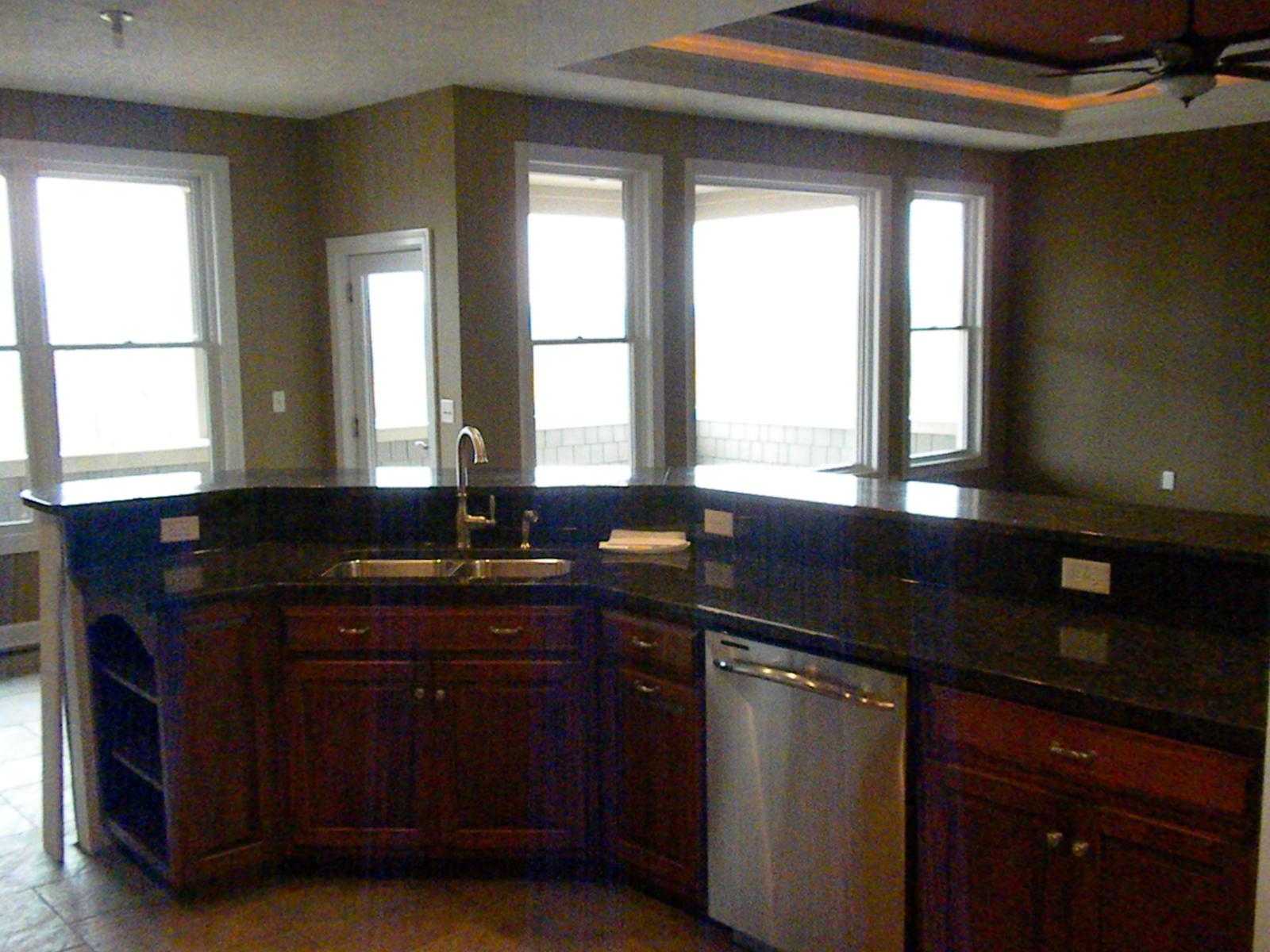 A kitchen island with a sink and dishwasher set into dark stone counters, windows behind opening to the ridge