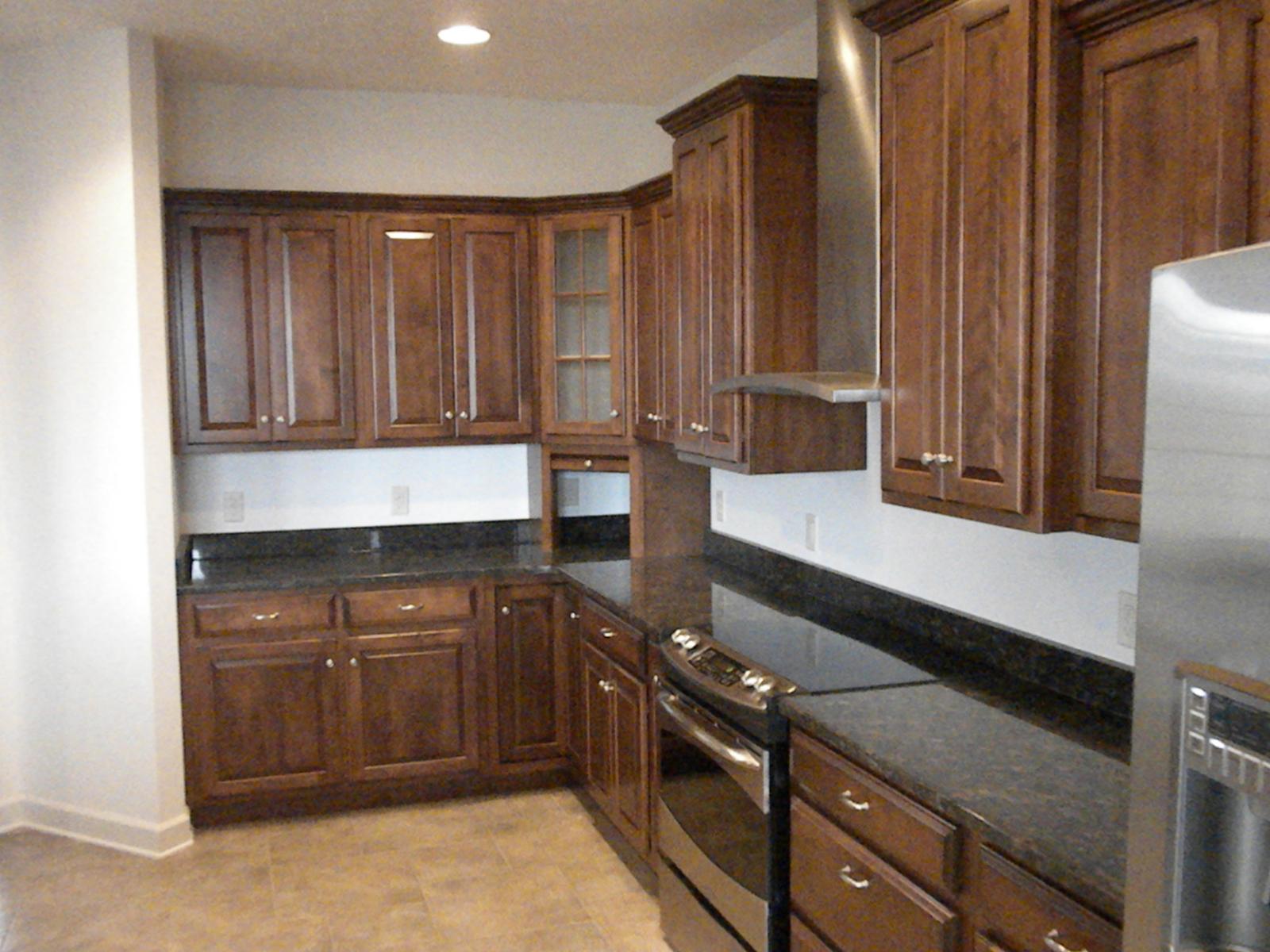 A kitchen corner with dark cabinets to the ceiling, a range under a hood and stone counters