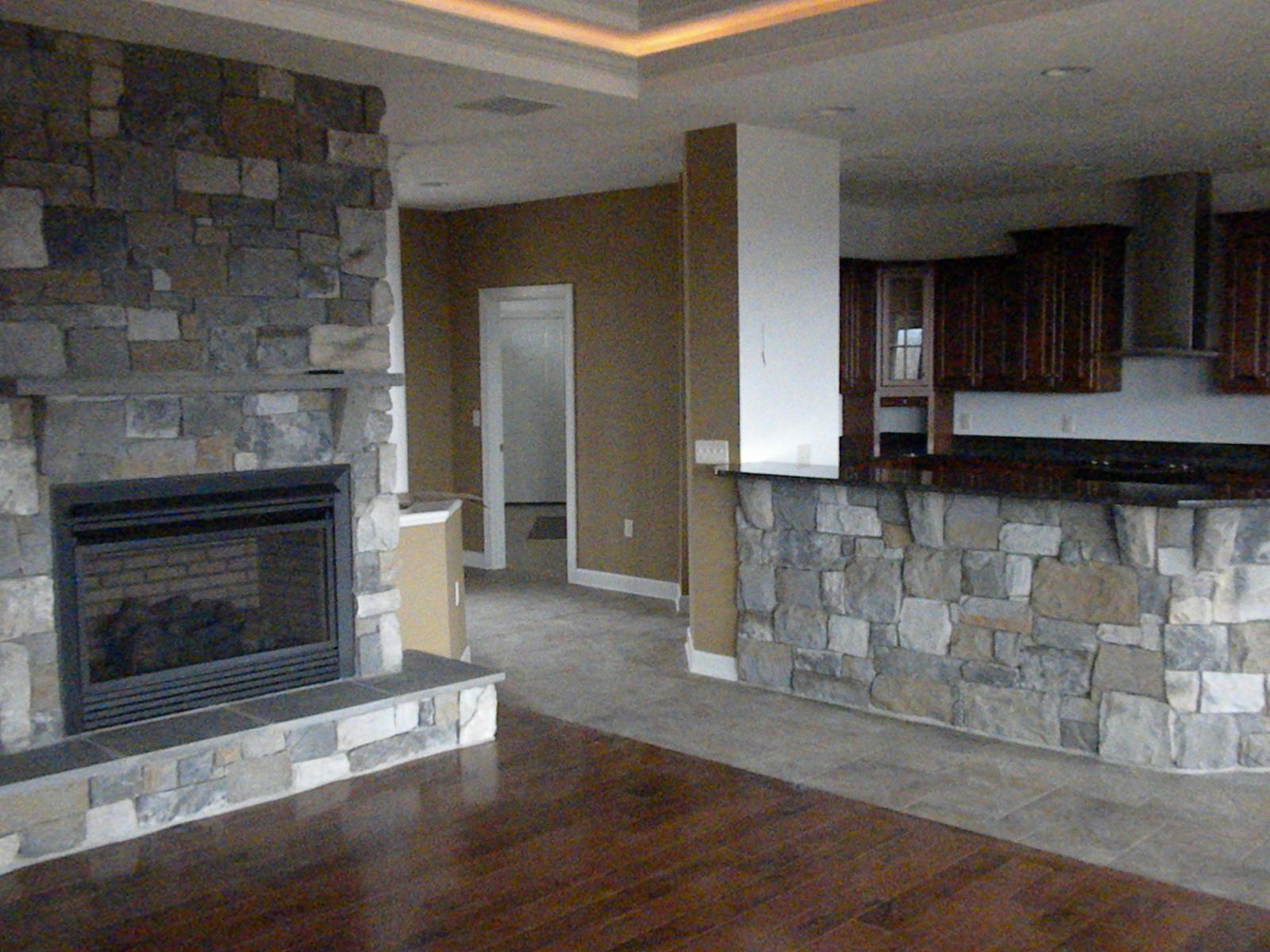 The great room and kitchen together, stone fireplace on the left and a tray ceiling picked out in cove lighting