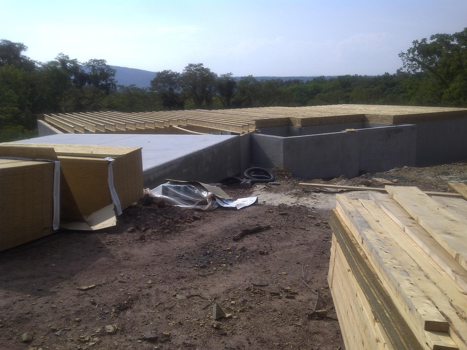 The deck and foundation from ground level, insulation board stacked beside the wall and lumber laid out ready