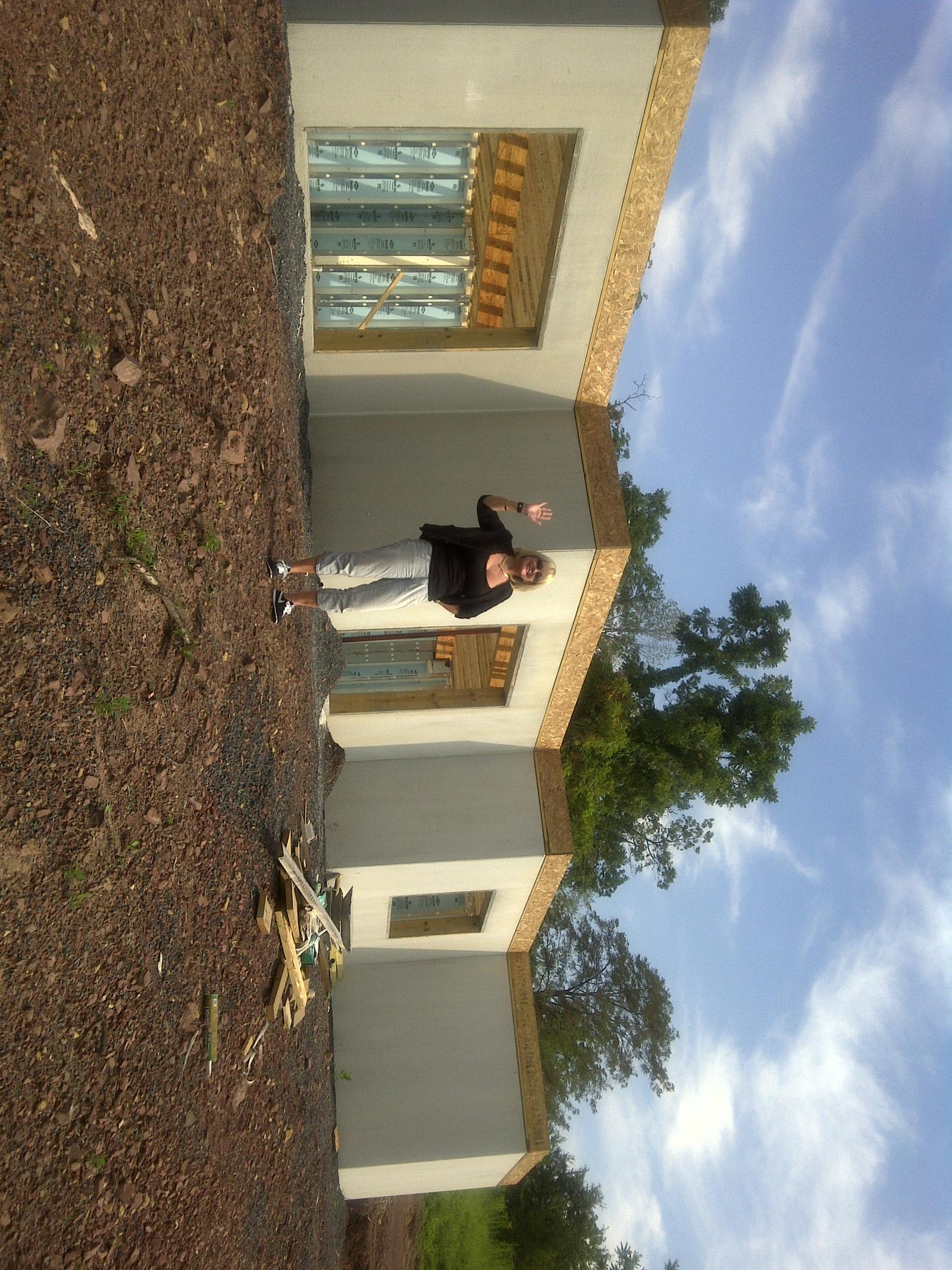 A person standing at the foundation wall with an arm raised toward the camera, sheathing laid along the top of the wall