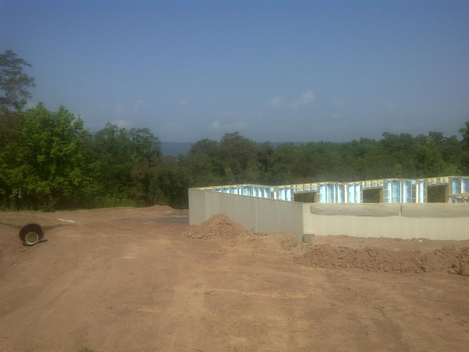 The finished foundation from the far end, earth banked against the near wall, treeline and haze behind