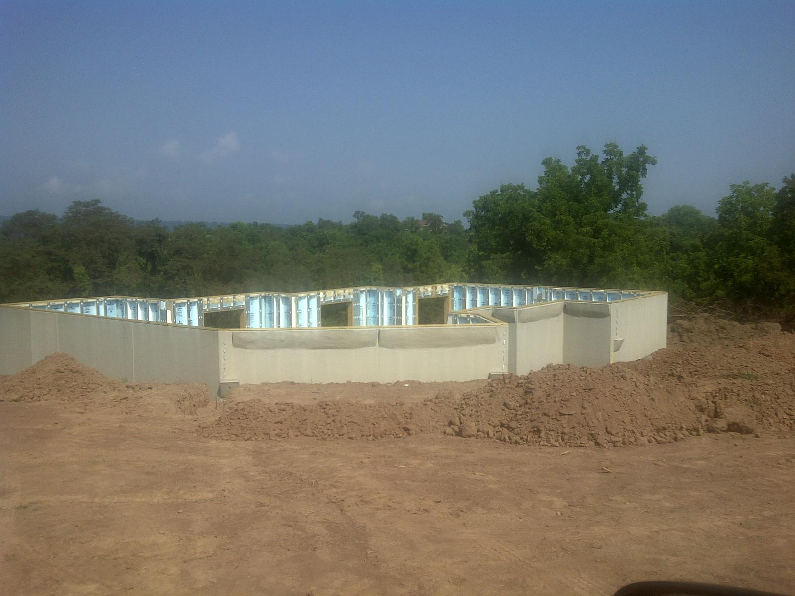 Foundation walls standing on the pad, precast panels with insulation showing between the ribs, the footprint stepping around its corners