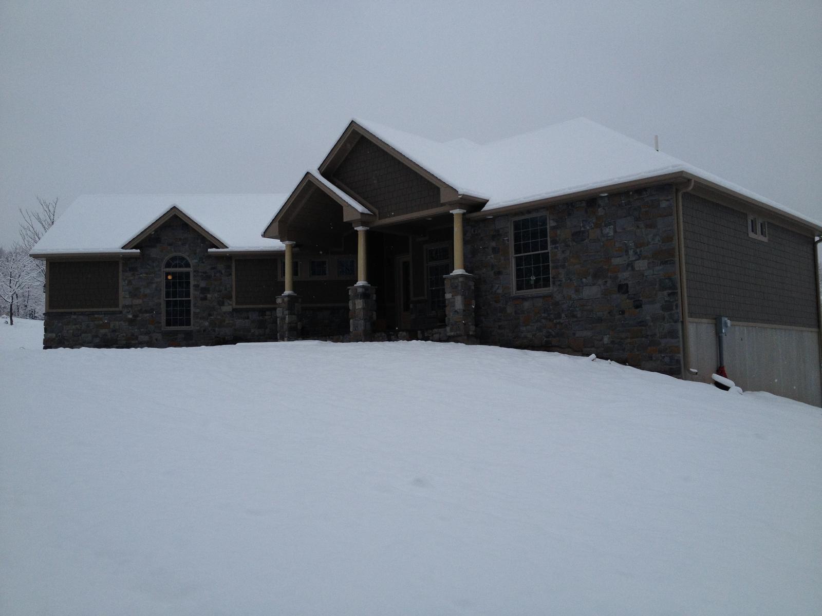 The house from the low side in snow, the walkout level showing under the main floor