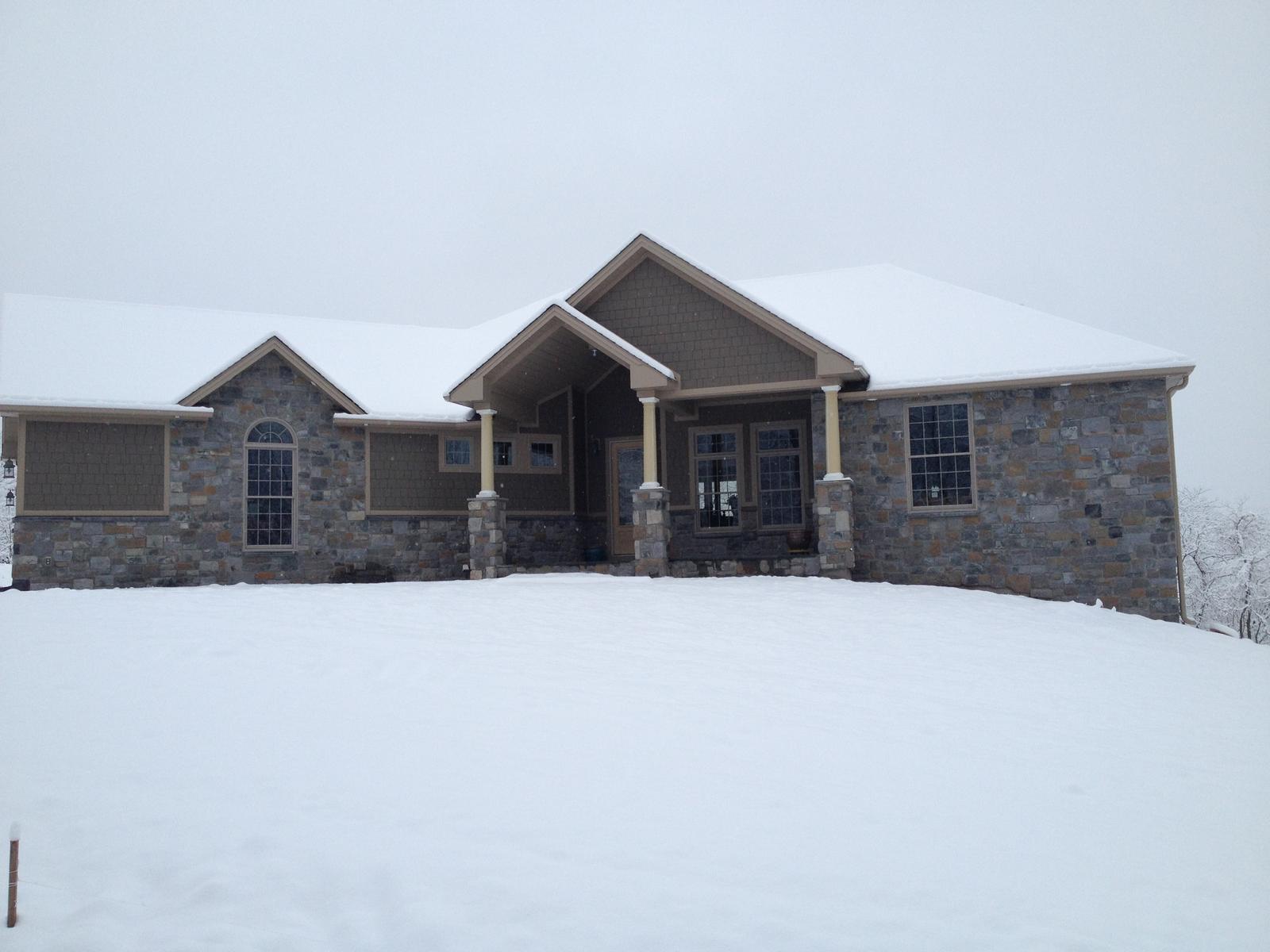 The house along its front in snow, porch columns and stone standing out against the white