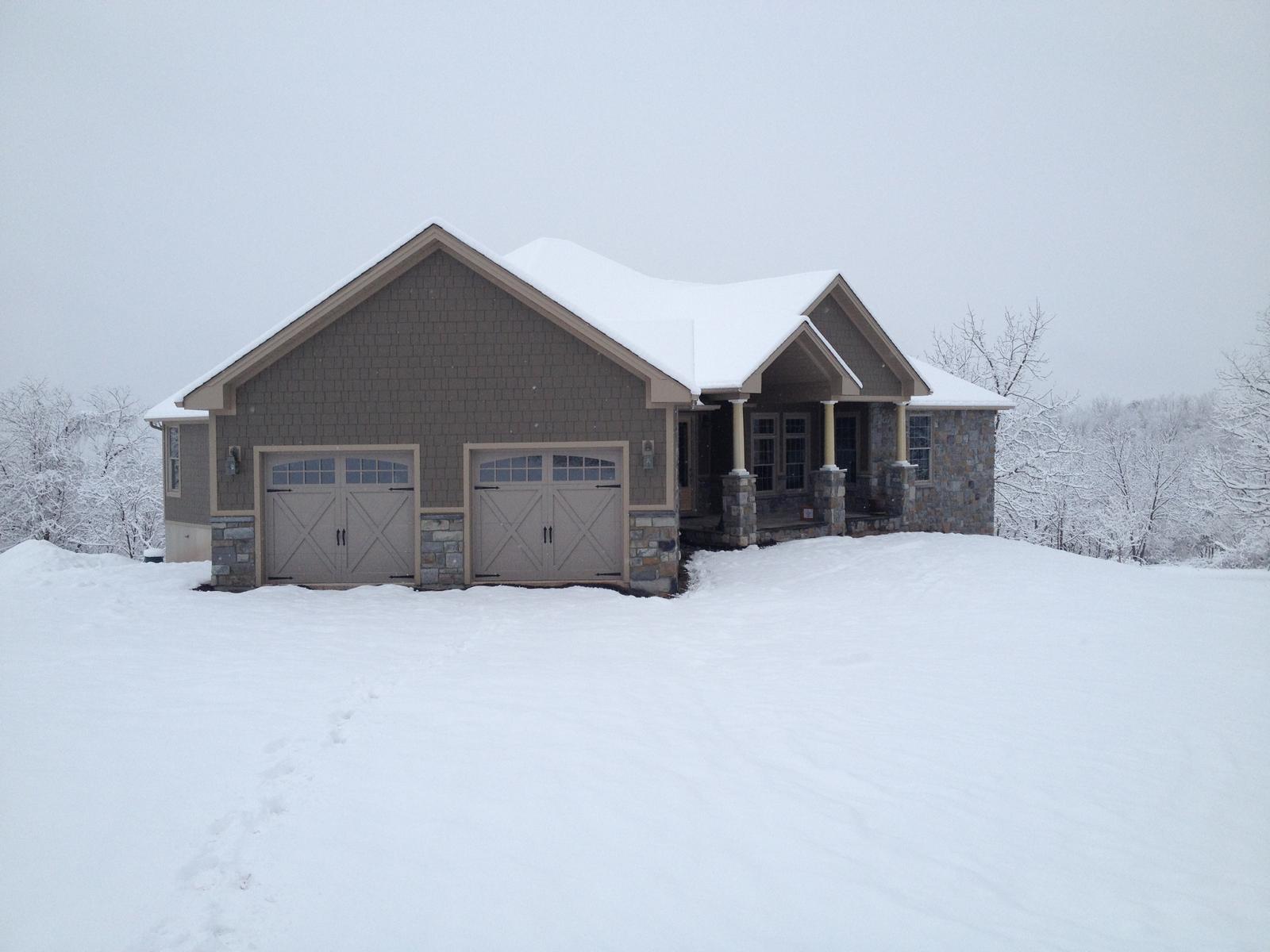 The garage doors and gable in falling snow, the house running back behind them