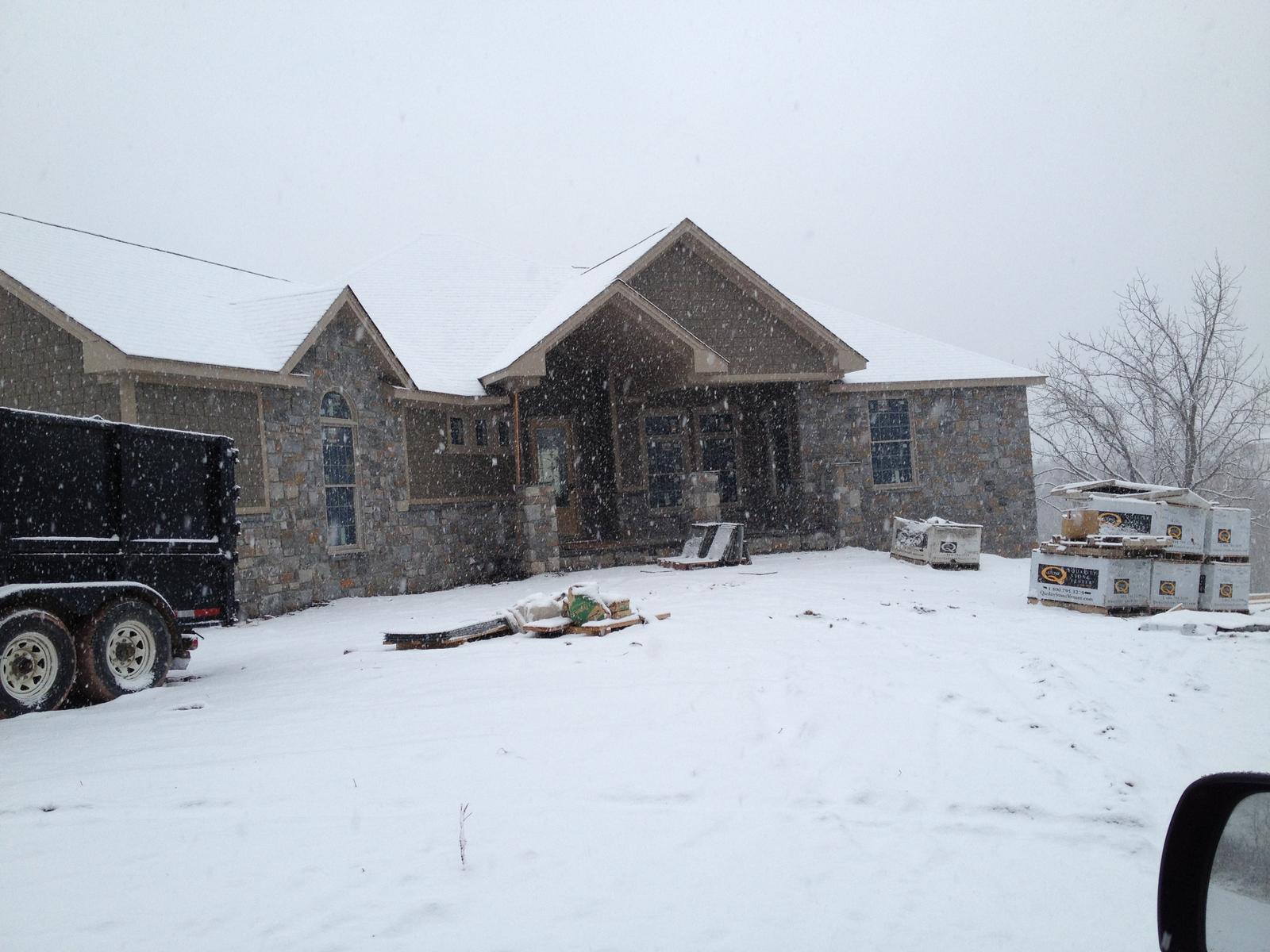 The house in falling snow, stonework complete and pallets of material still standing in the yard