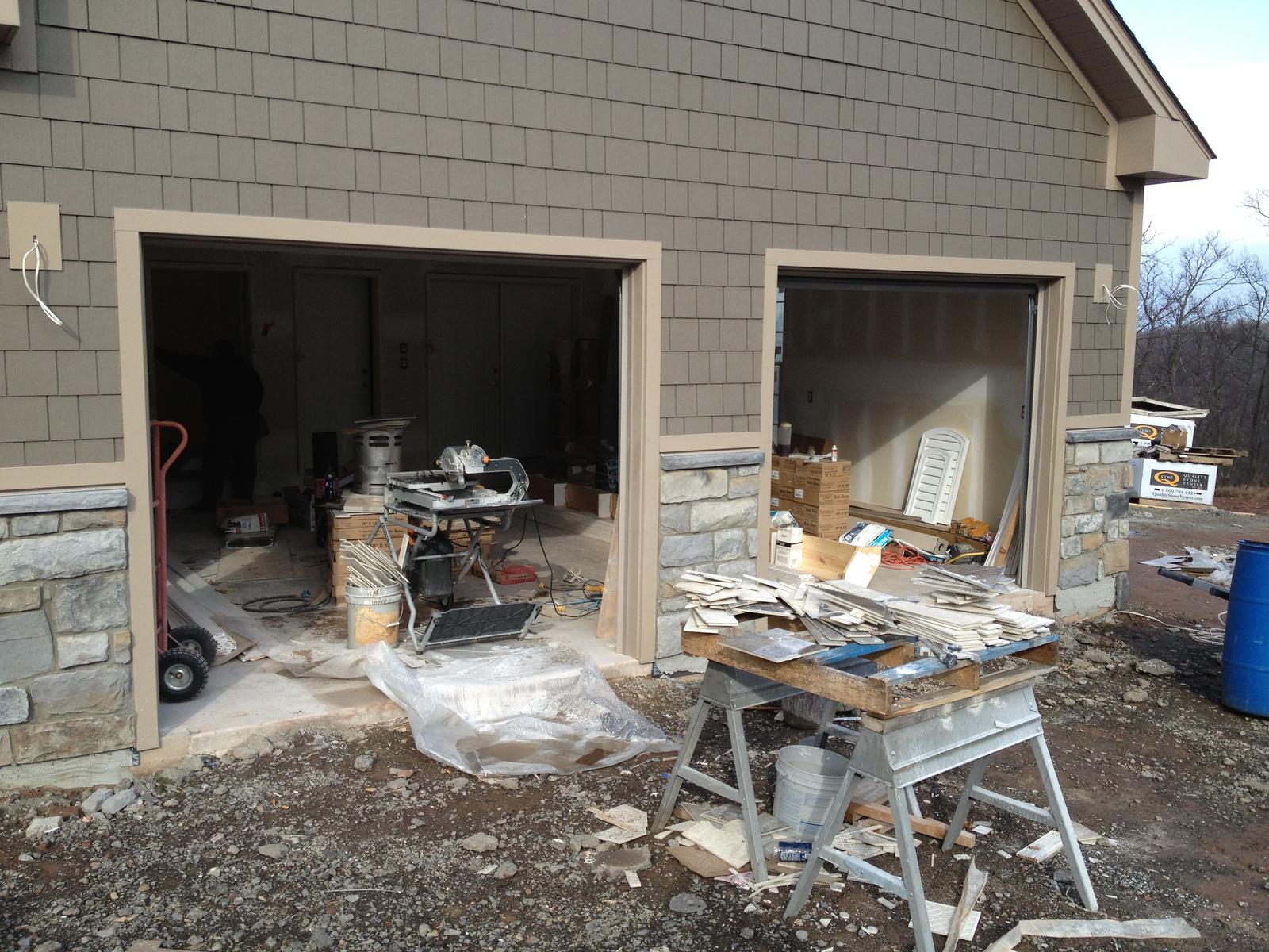 Two open garage bays with tools and materials inside, a workbench set up in the doorway