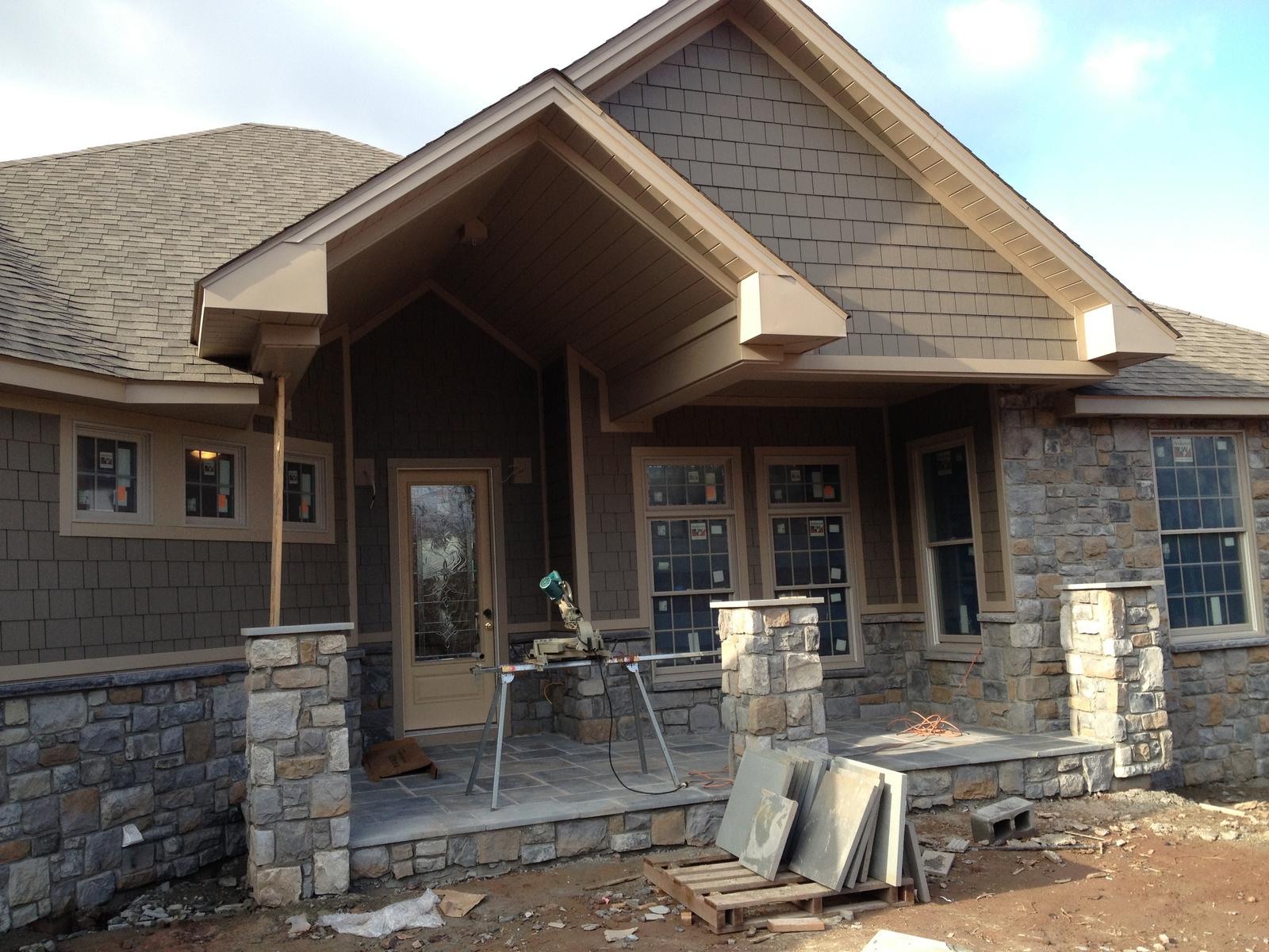 The entry front with its gable and columns, stonework going up and flagstone stacked ready on the ground
