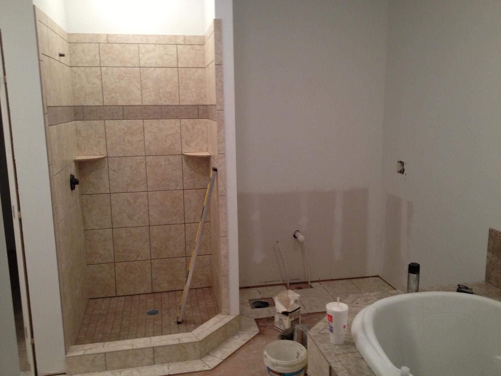 A tiled corner shower with recessed shelves, a tub set beside it and drywall still bare