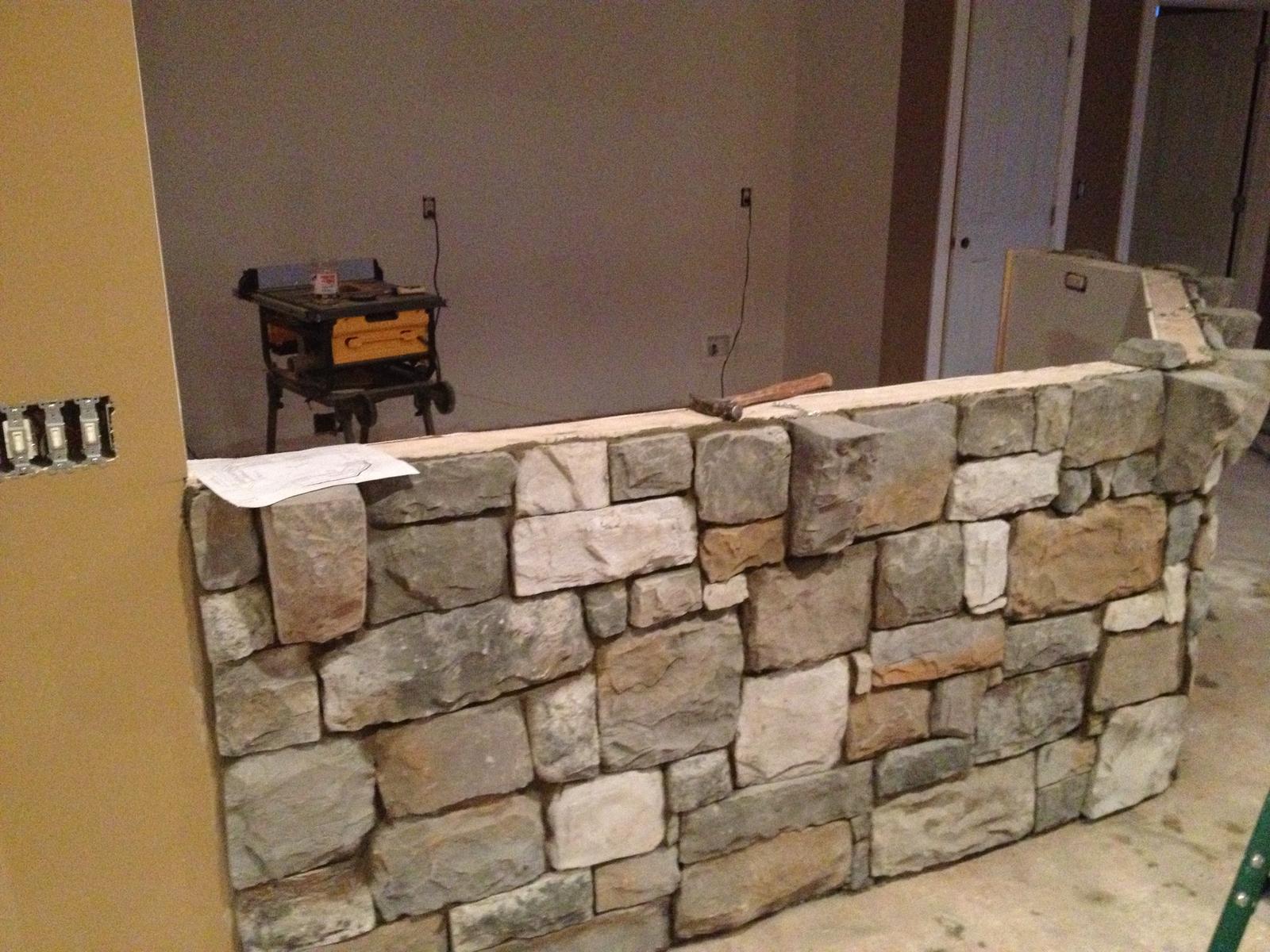 A stone knee-wall being laid across a room, tools and a work light standing beyond it