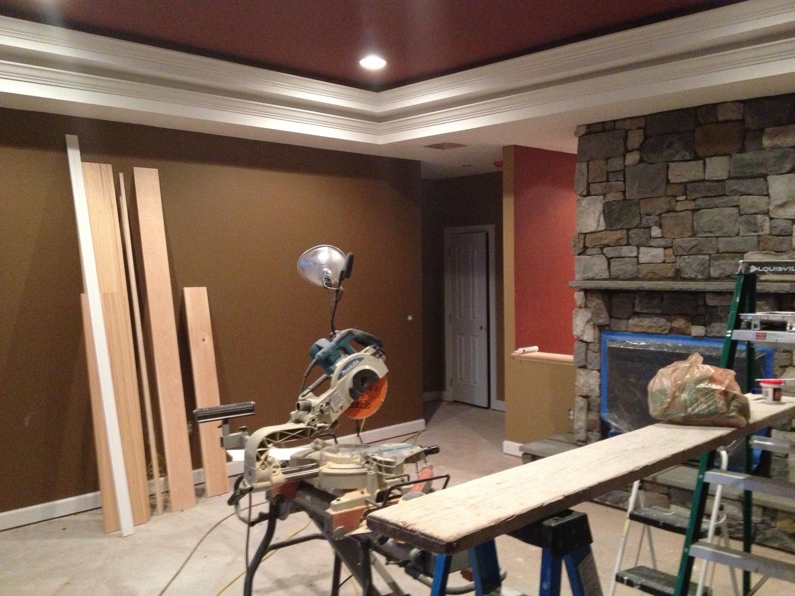 A room in finishing, a miter saw set up on the floor and trim stacked against the wall beside the stone chimney