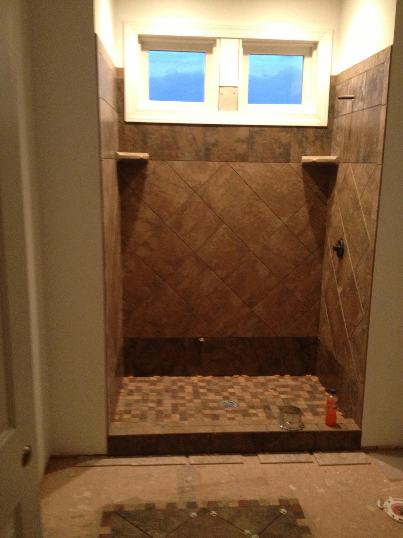 A tiled shower under construction, glass block windows above and a tiled floor laid to the drain