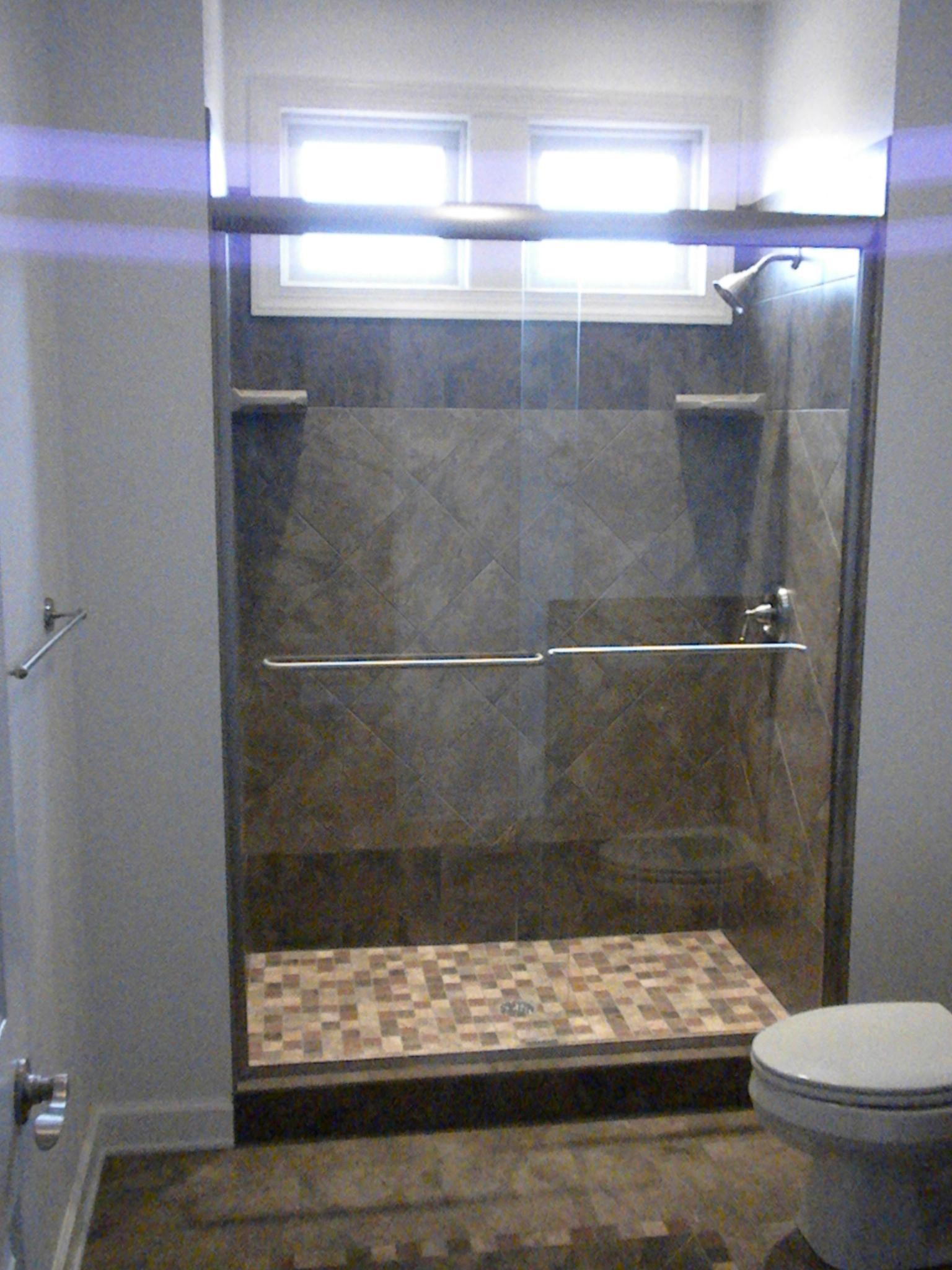 A large tiled shower behind glass, twin heads and a patterned tile floor