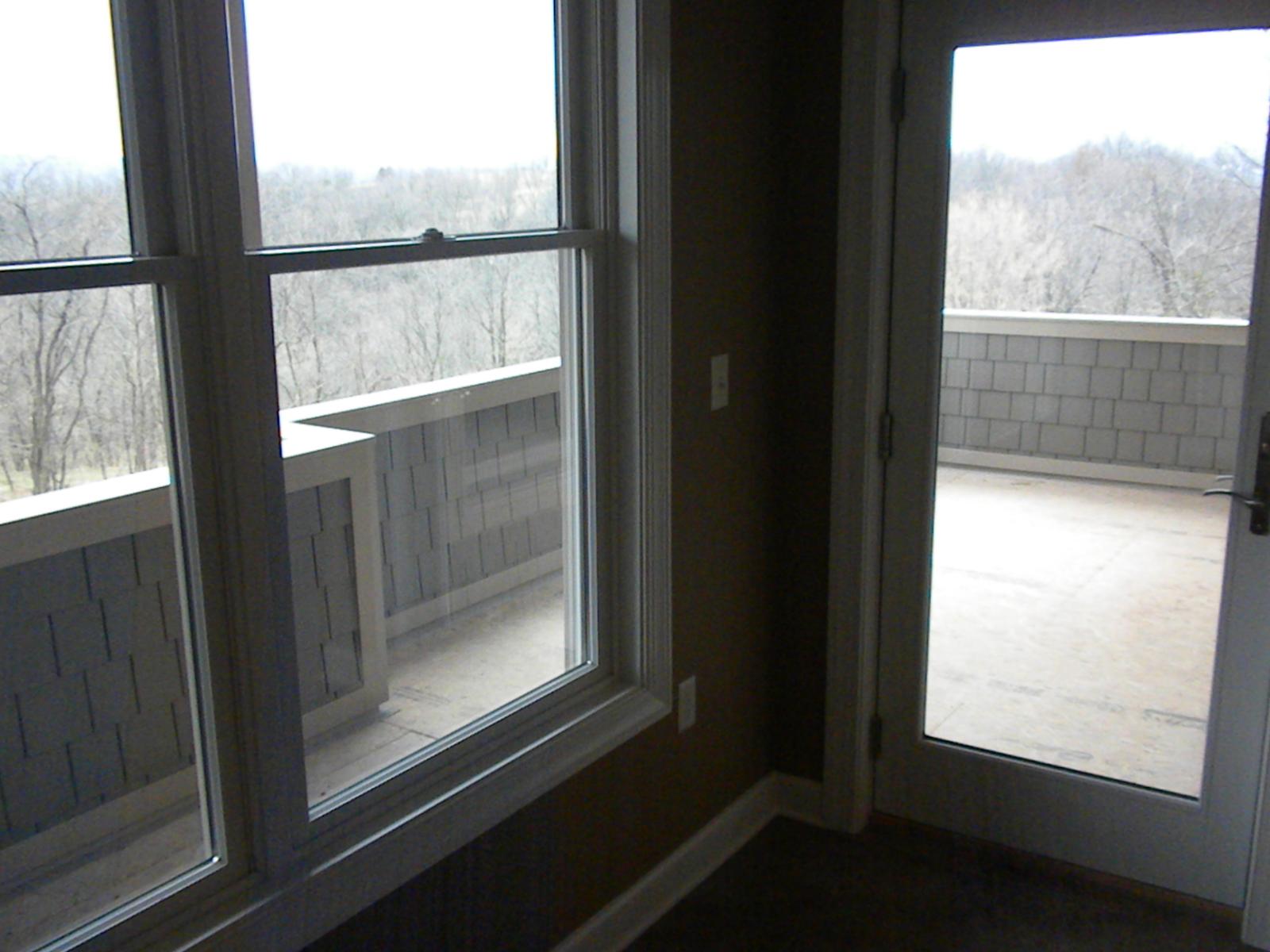 A corner of a room with tall windows and a glazed door opening onto a covered porch