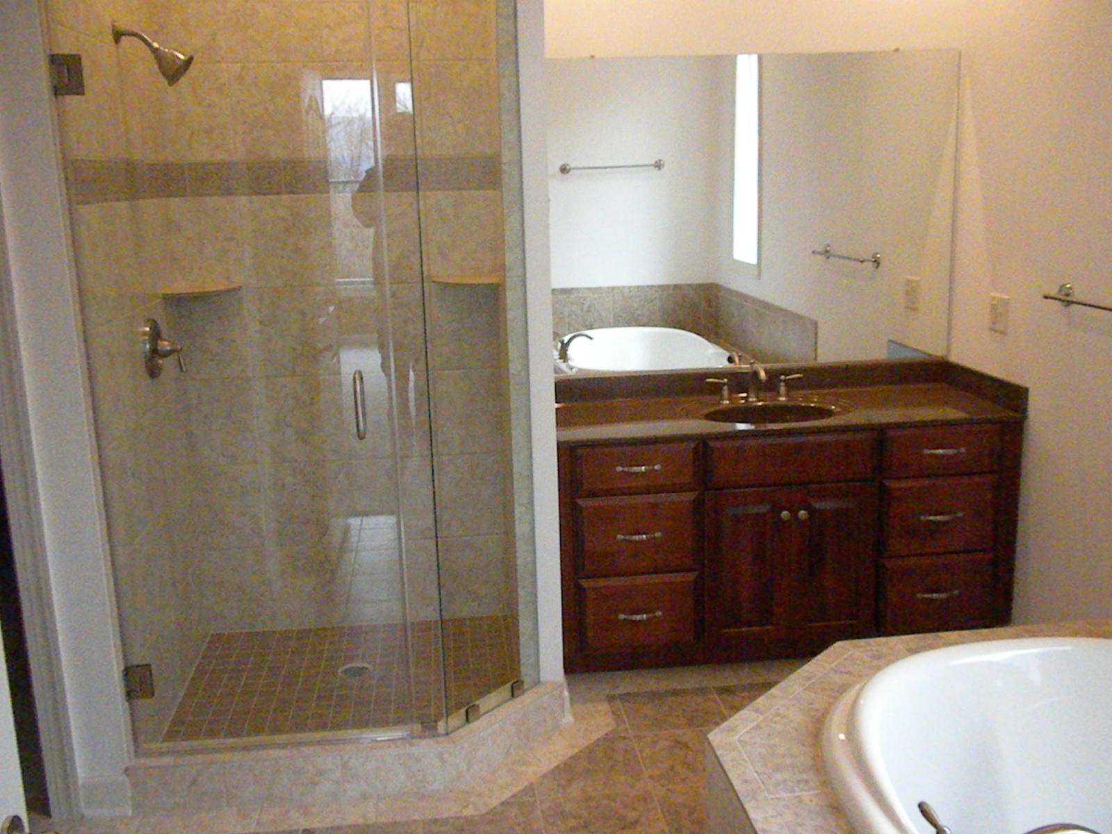 A bathroom with a glass corner shower, a tiled tub deck and a dark vanity between them