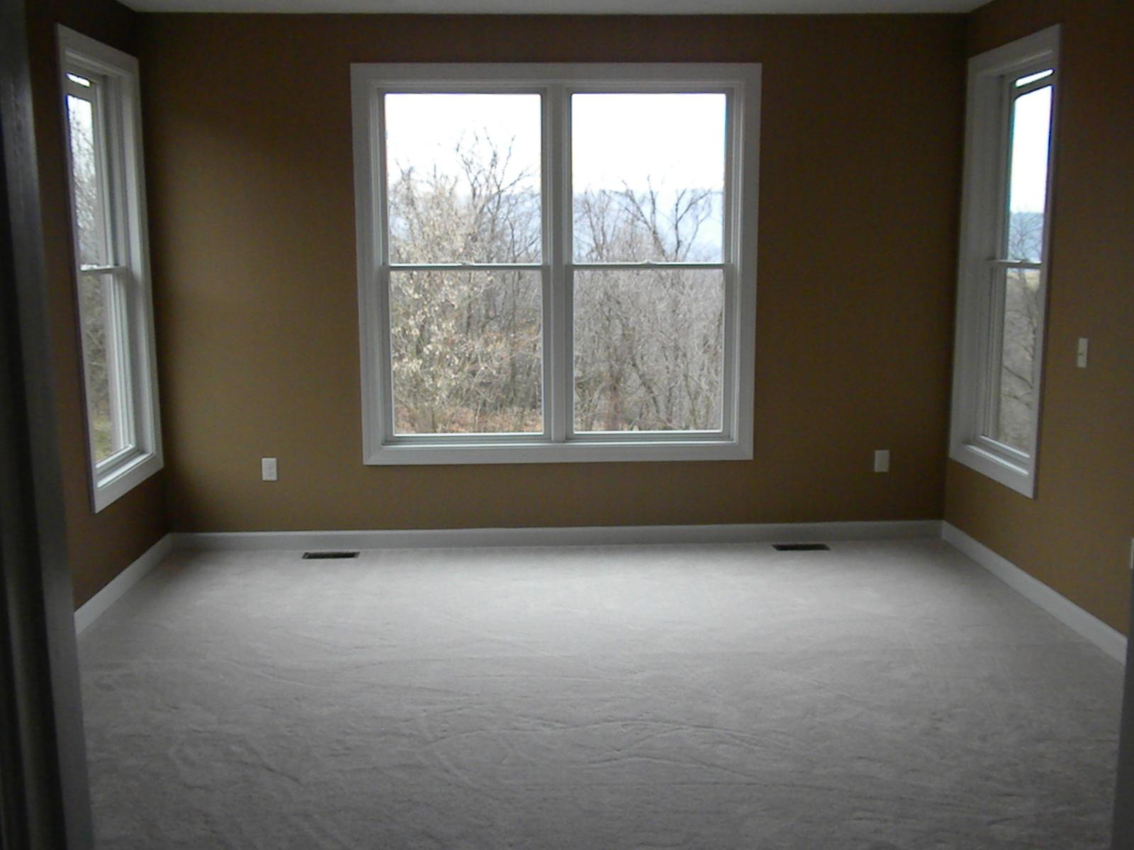 An empty bedroom with three windows and taupe walls, bare floor waiting for covering