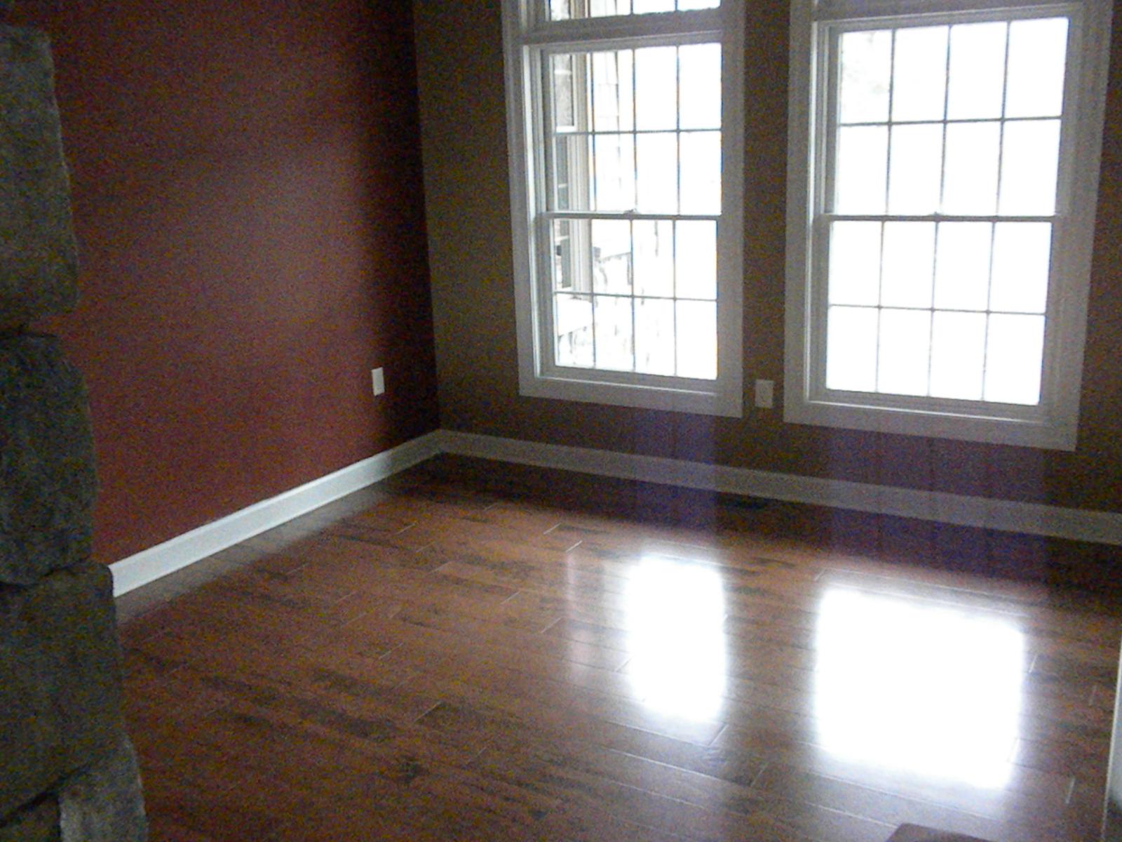 A room with dark red walls and two tall windows, low sun striking the new wood floor