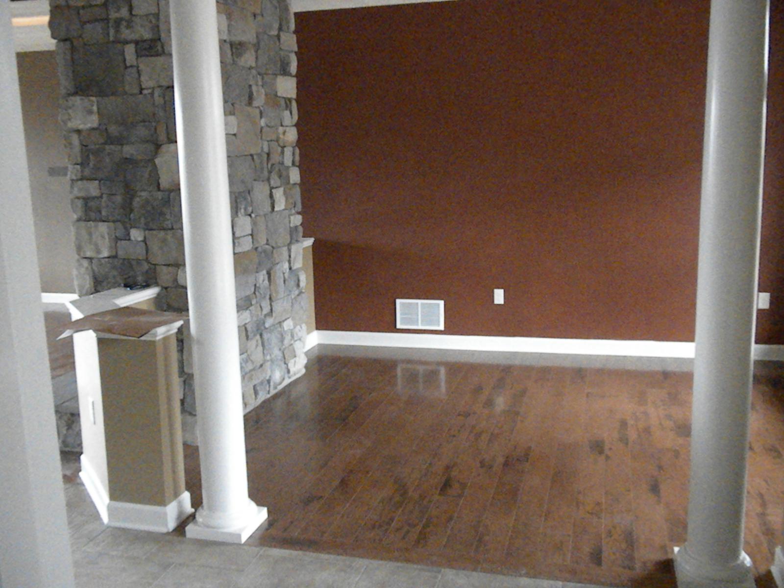 A stone chimney breast beside a deep red wall, a white column at the corner and new wood flooring running away from it