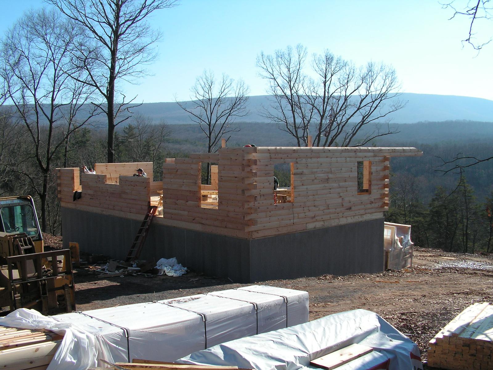 The same walls from further back, courses laid to window height and a ladder against the corner