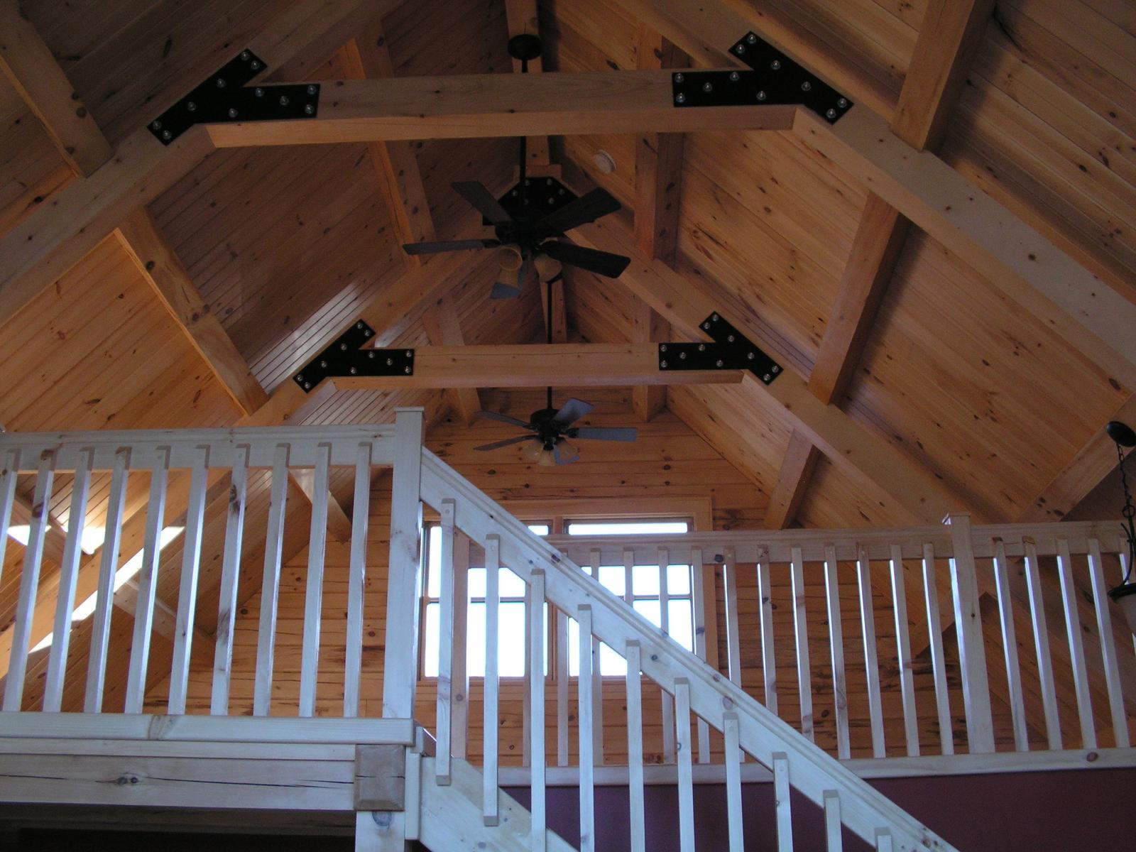 The open roof structure from below, trusses and collar ties joined with black plates above a stair rail