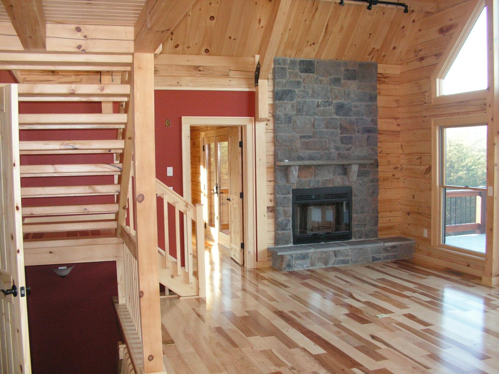 The great room from the stair, stone chimney breast rising past a gable window and red walls beside it