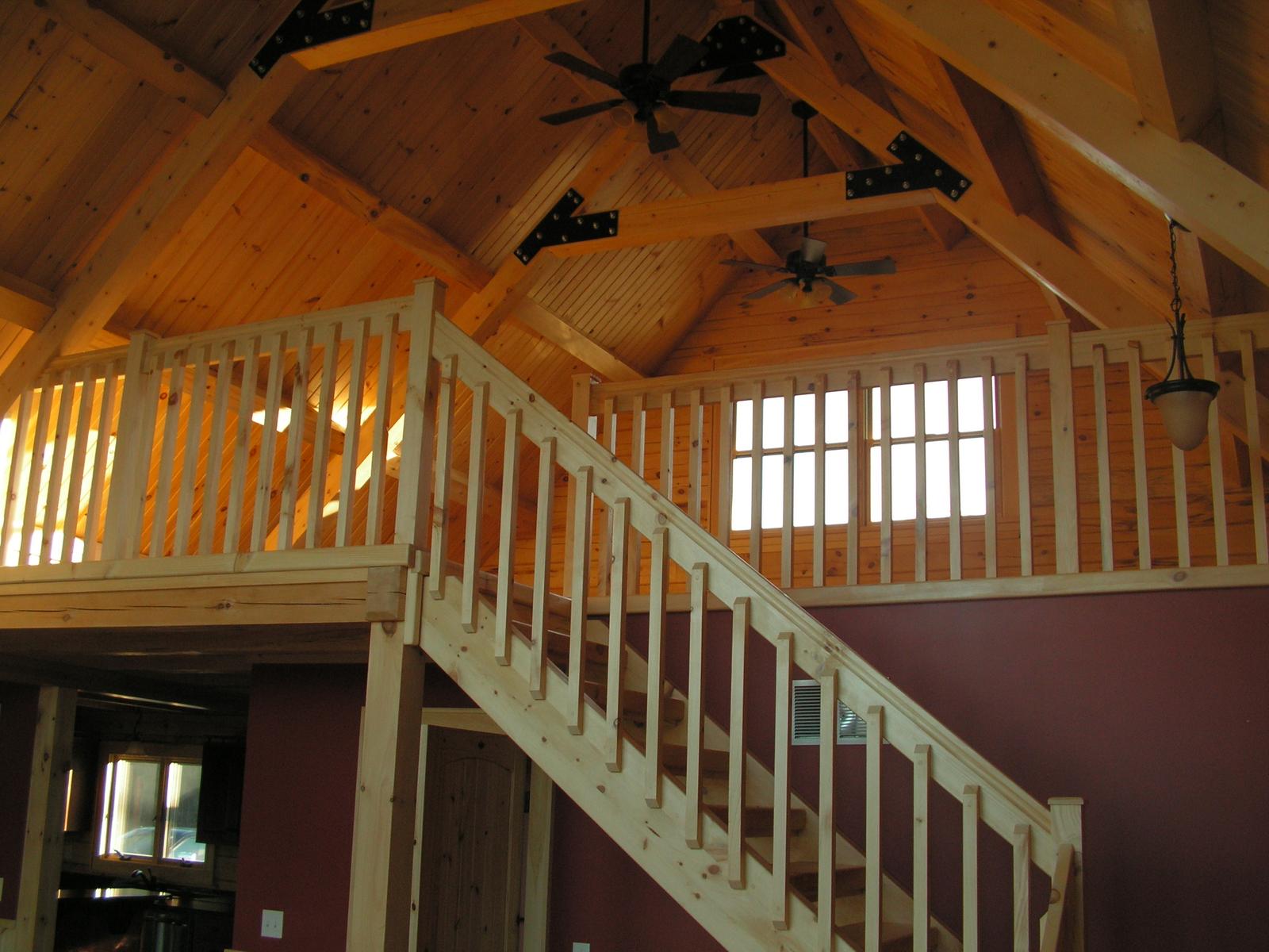 A loft stair and railing under an open timber roof, heavy trusses joined with black steel plates