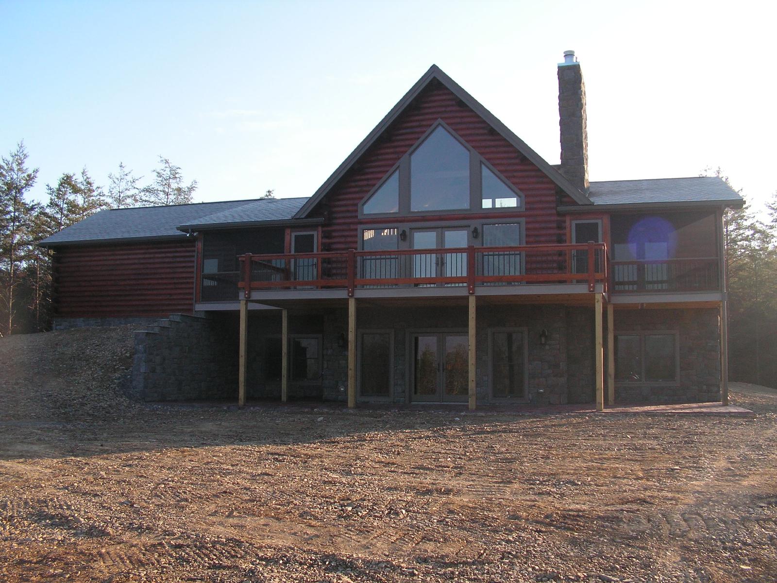The home from the open side, gable glass centered above a railed deck and the lower level opening beneath