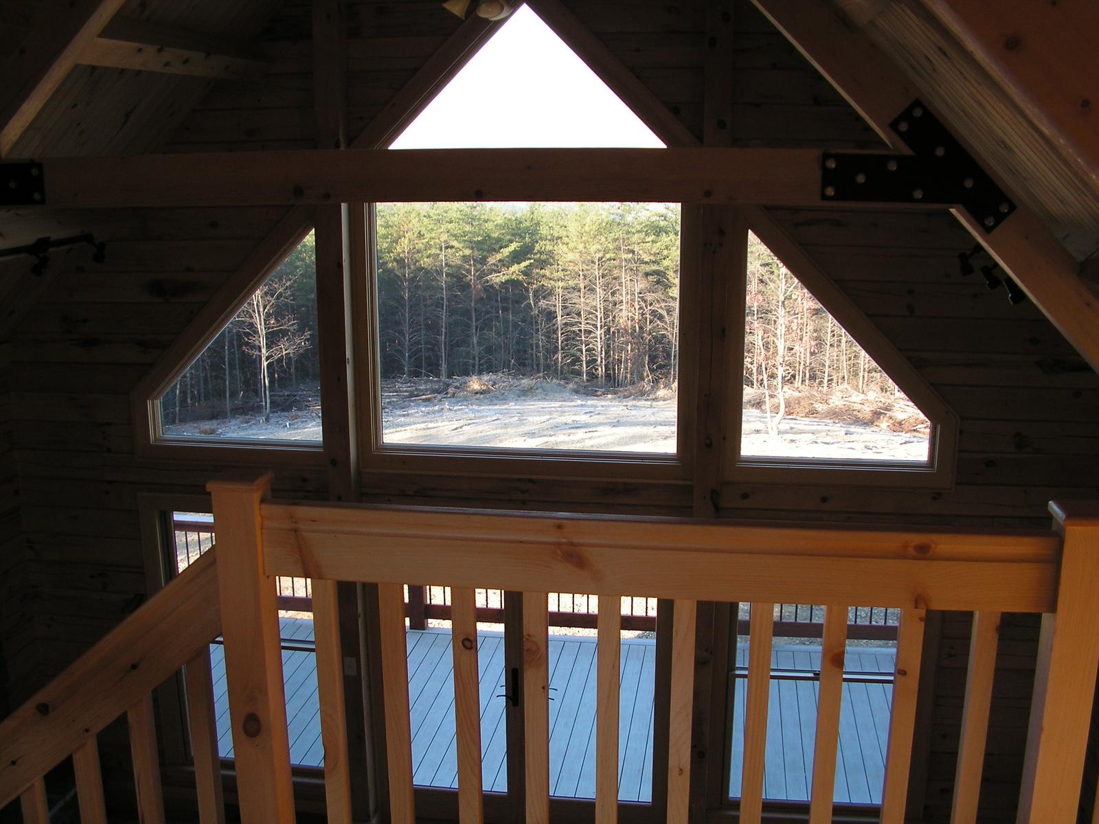 The loft rail against three gable windows, snow-covered woods showing through the glass