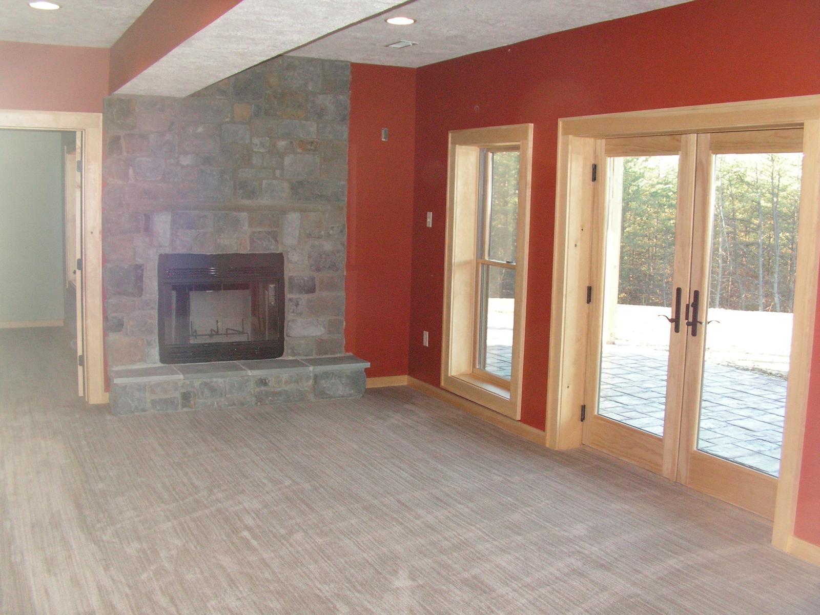 A lower-level room with a stone fireplace, glazed doors along one wall and red walls around