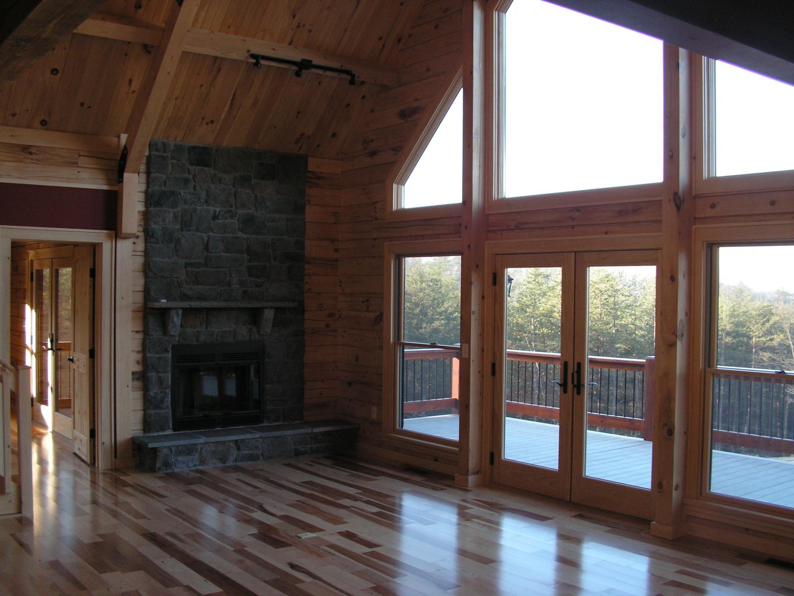 A great room with a stone fireplace at one end and glazed doors along the wall opening to a deck