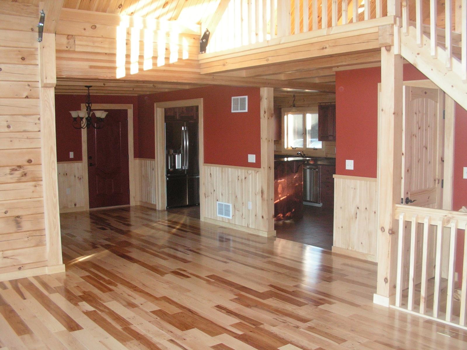An entry hall with red walls above a board wainscot, wood floor running through to a kitchen beyond