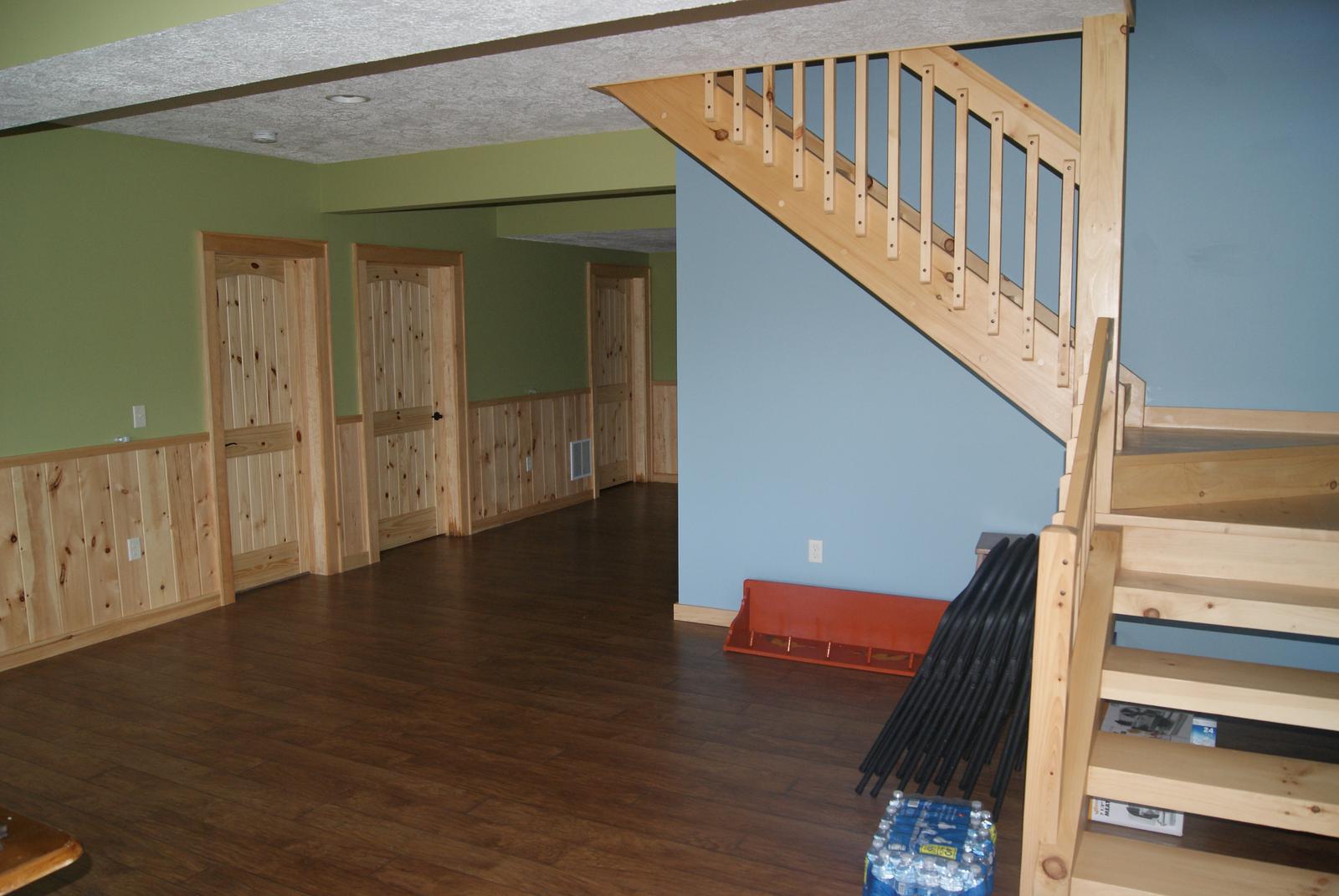 A lower-level room with a board wainscot under green and blue walls, a stair running down at one end