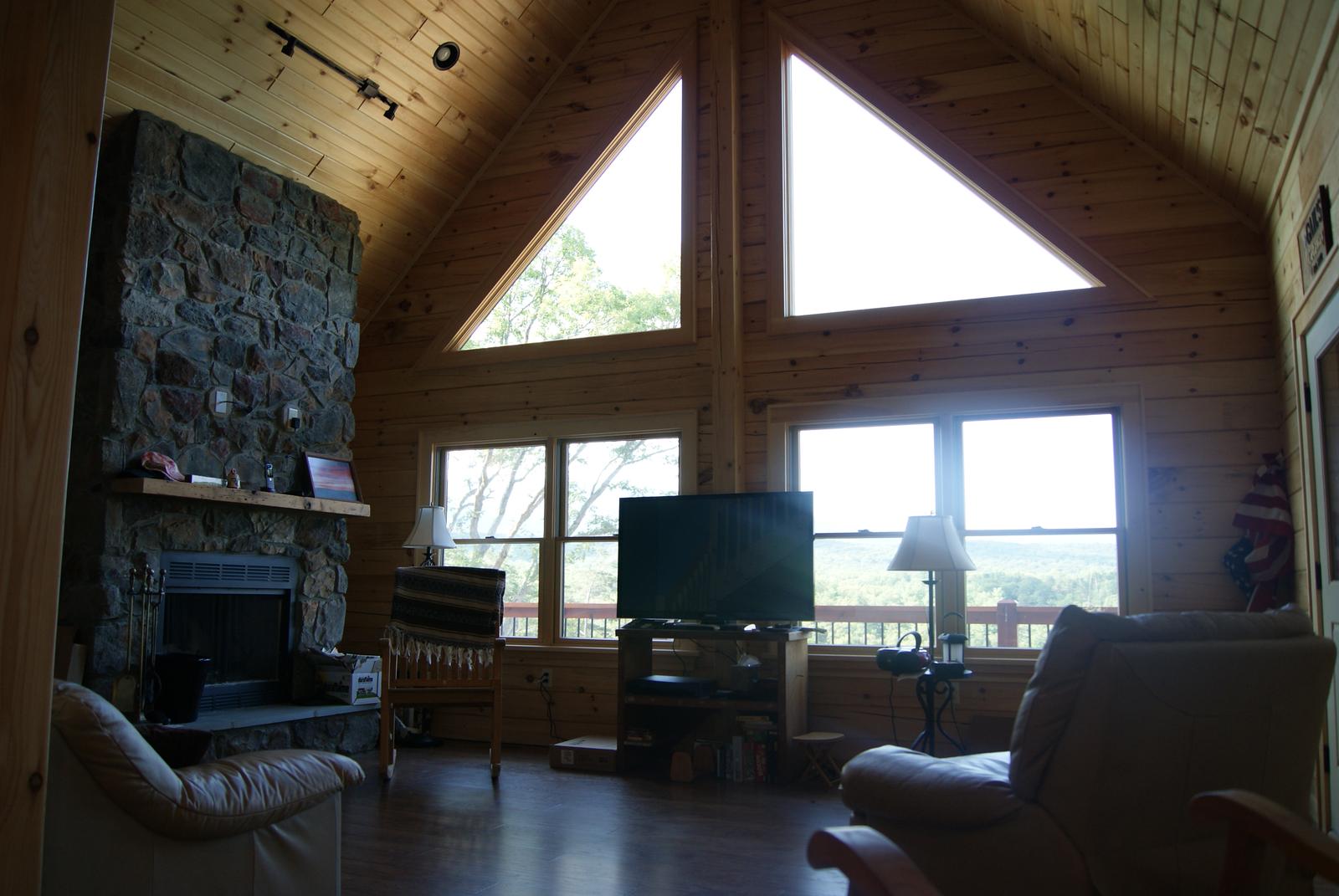 A great room under a vaulted board ceiling, twin triangular gable windows above a wall of glass