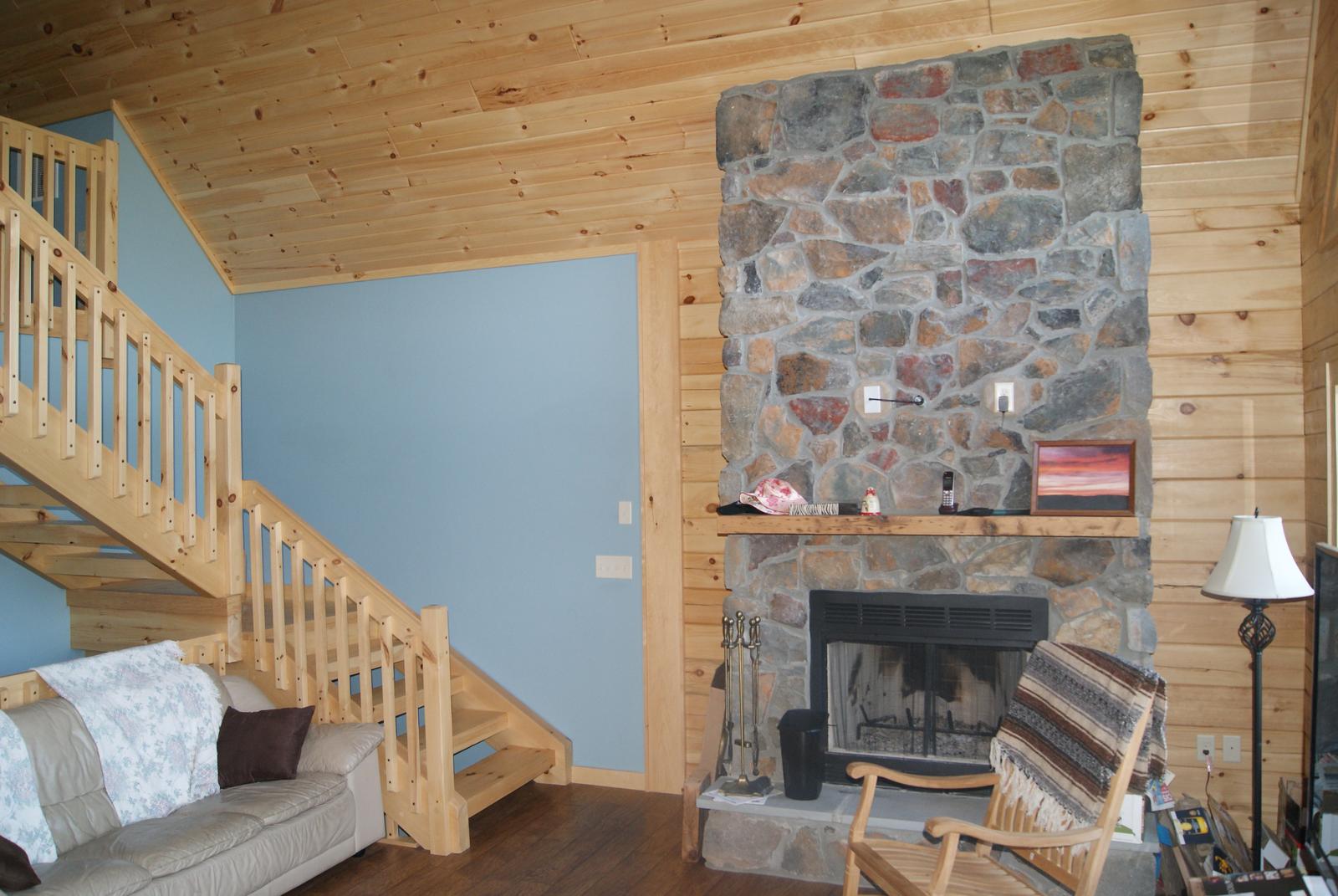 A stone fireplace with a timber mantel between a stair and a window, board walls either side
