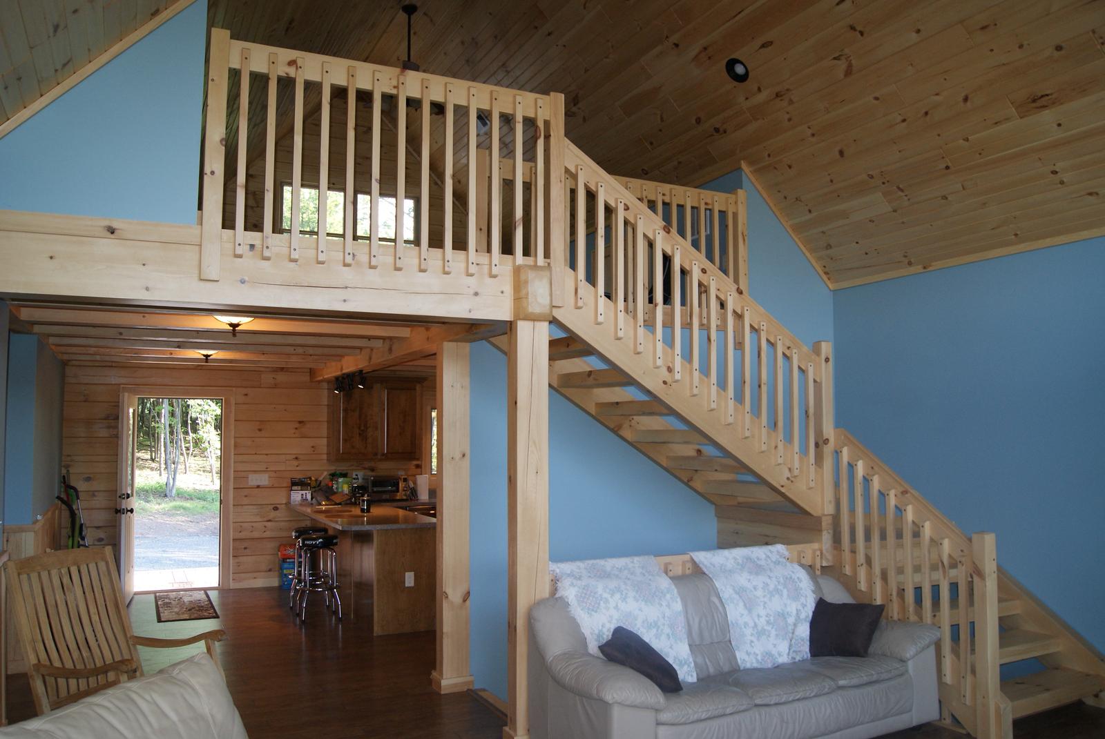 A stair and loft rail seen from the room below, board ceiling sloping above pale blue walls