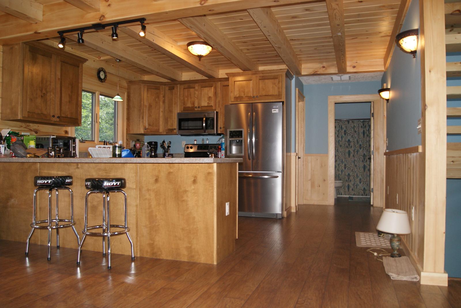 A kitchen with wood cabinets and a breakfast bar with stools, board ceiling and track lighting above