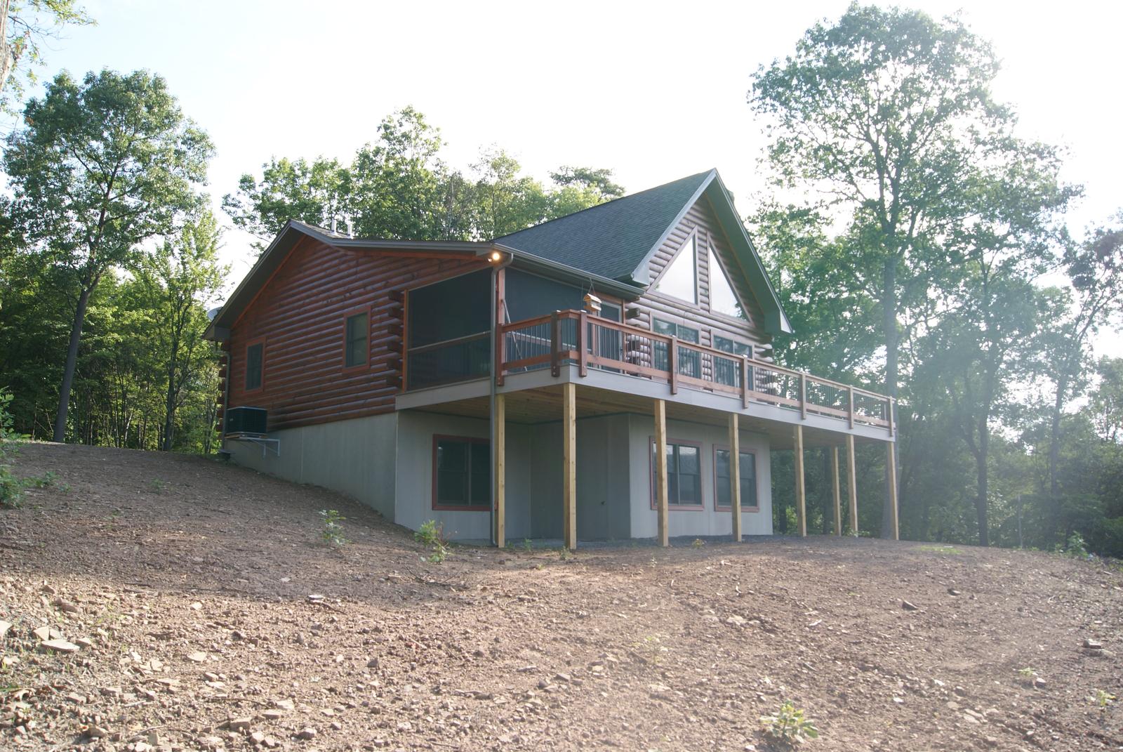 The home in flat light with the deck wrapping the near corner, freshly graded earth in front