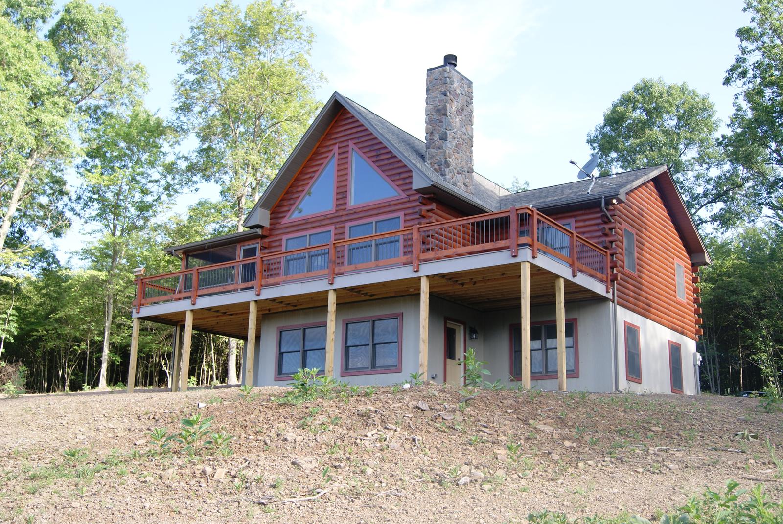 The home from the corner, a stone chimney running past the eaves and a gable of glass above the deck