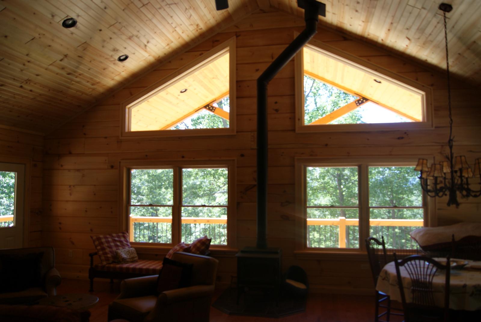 Two triangular gable windows above a wall of glass, the stove flue running up between them