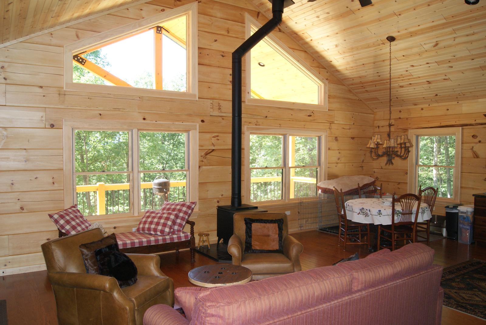 A great room under a vaulted board ceiling, a stove with a black flue and a gable window above the seating