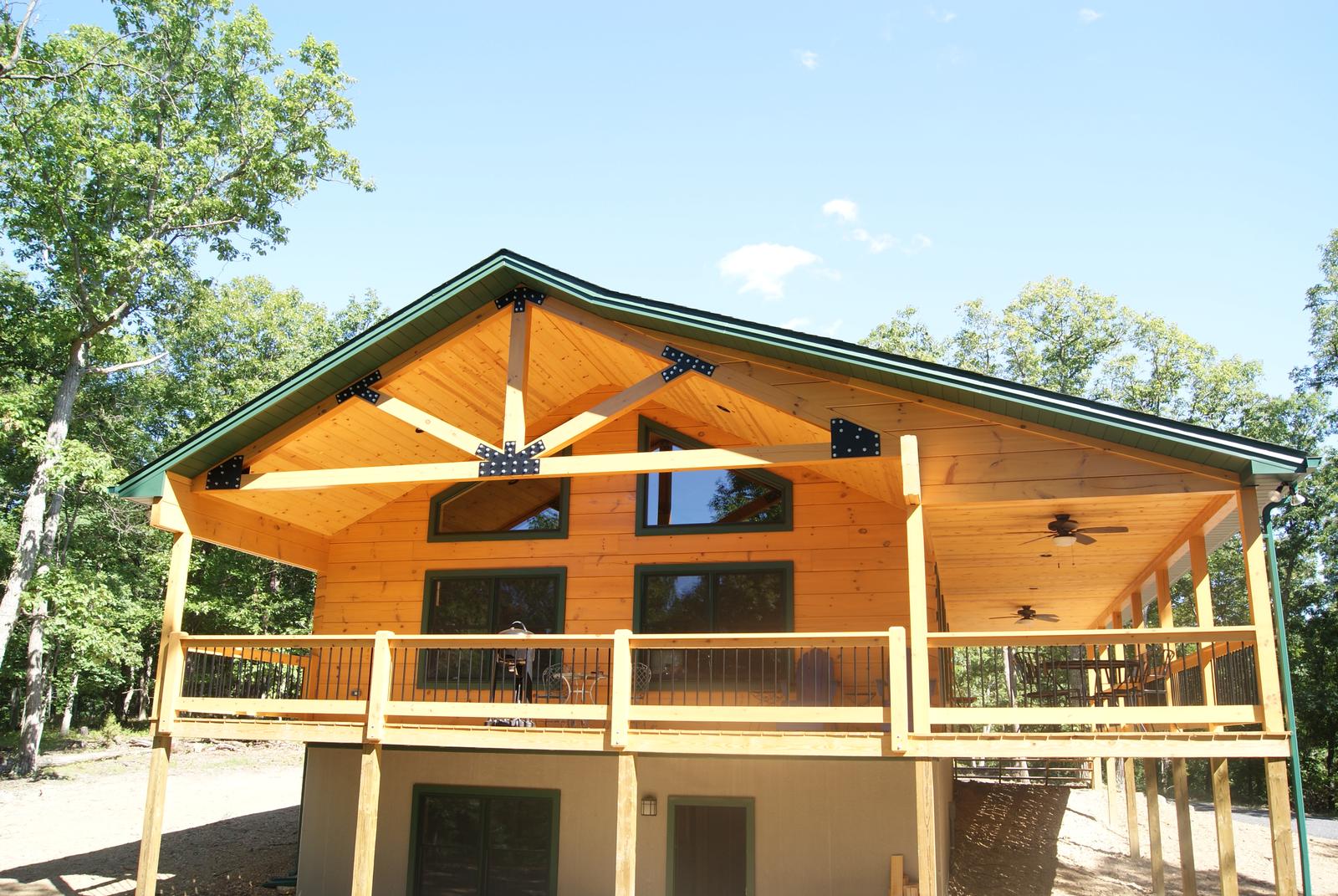 A log home with a deep covered porch, a timber truss on black steel plates in the gable above the rail