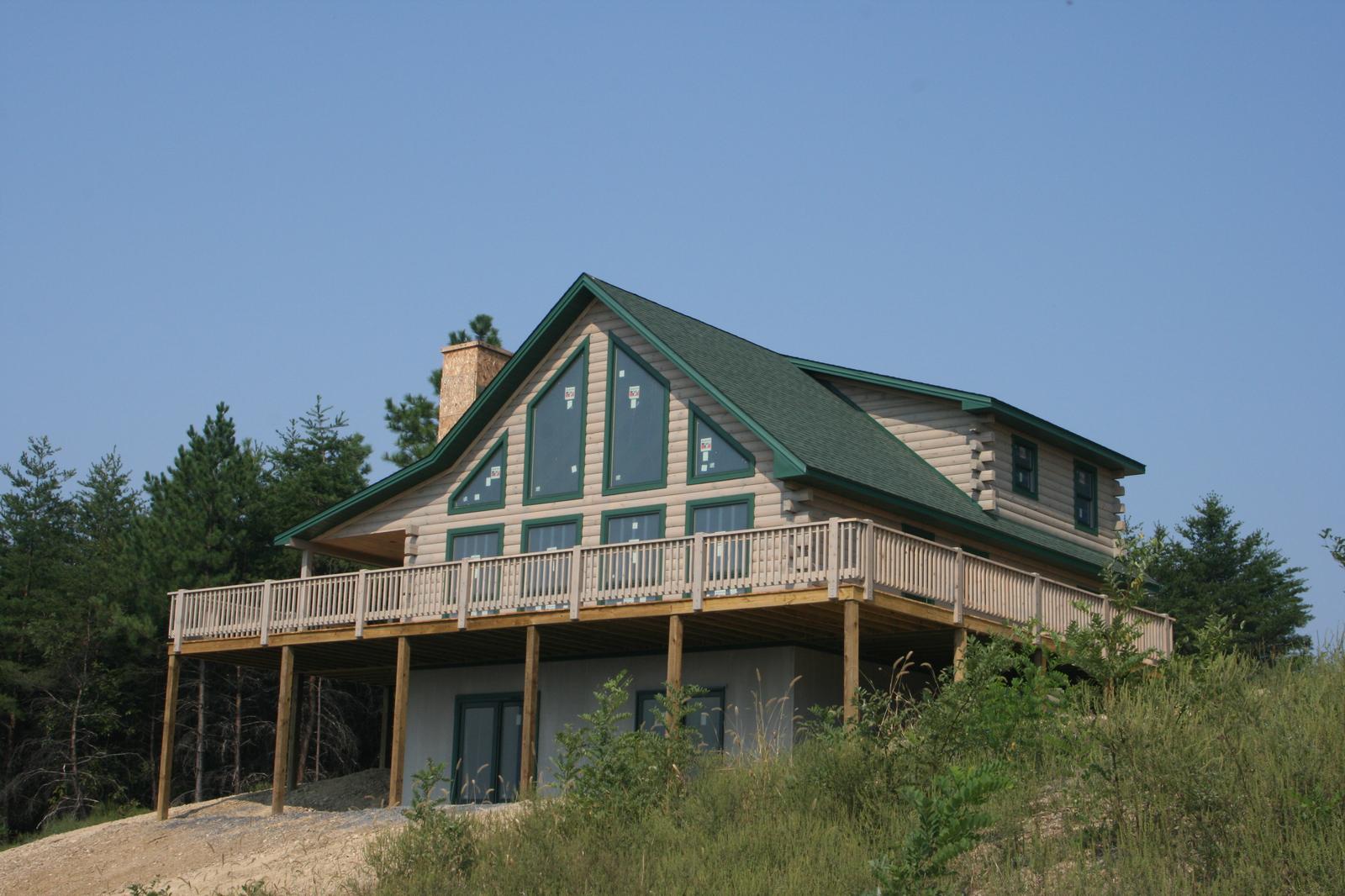 The same home from further back, stone chimney at the ridge and the deck running the full width