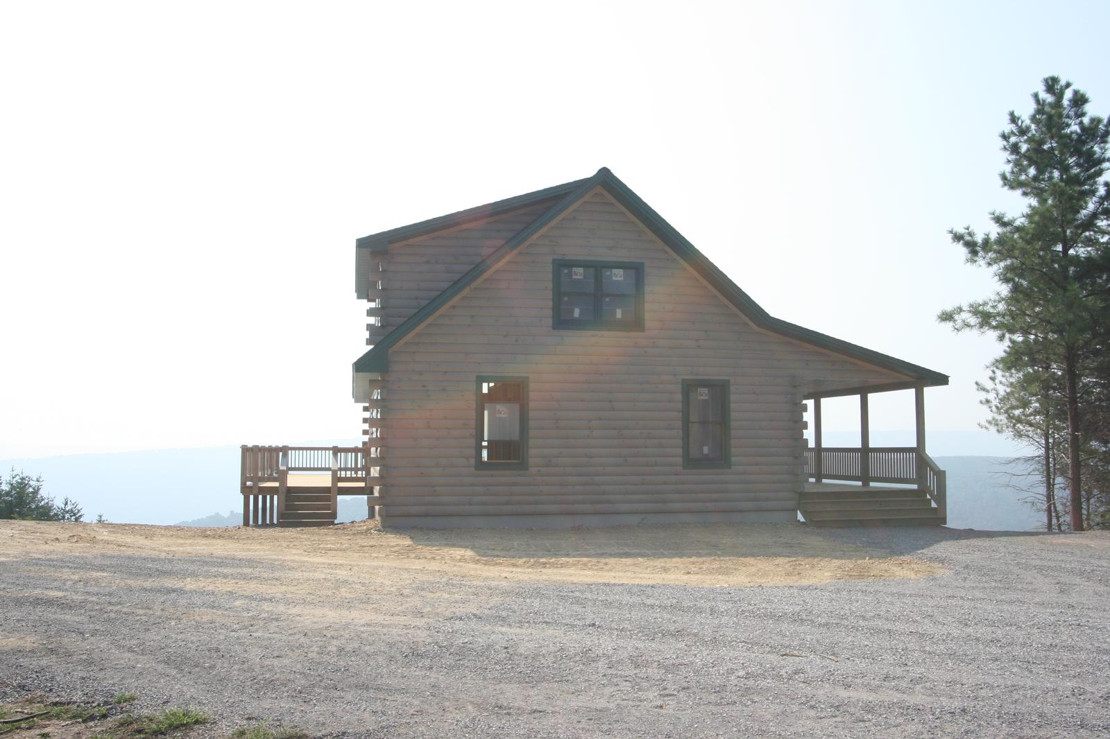 A log home in flat light with a covered porch to one side, gravel turning circle in front