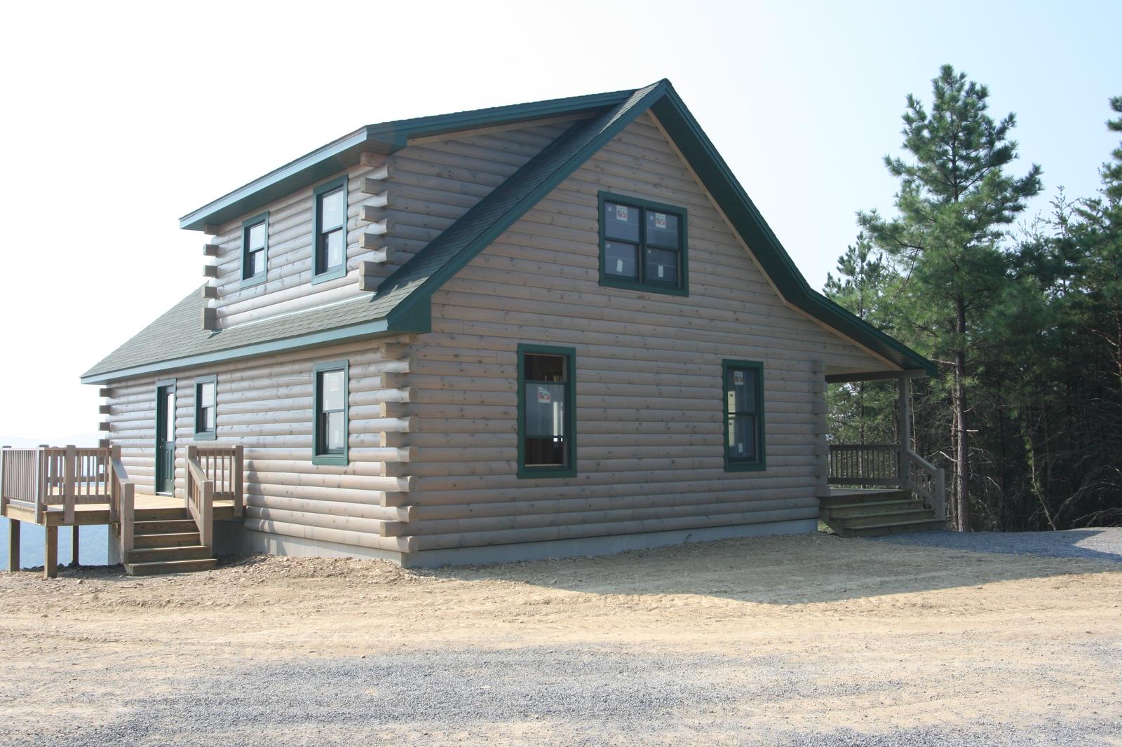 A log home from the corner, green roof and green-trimmed windows above a deck with a stepped entry